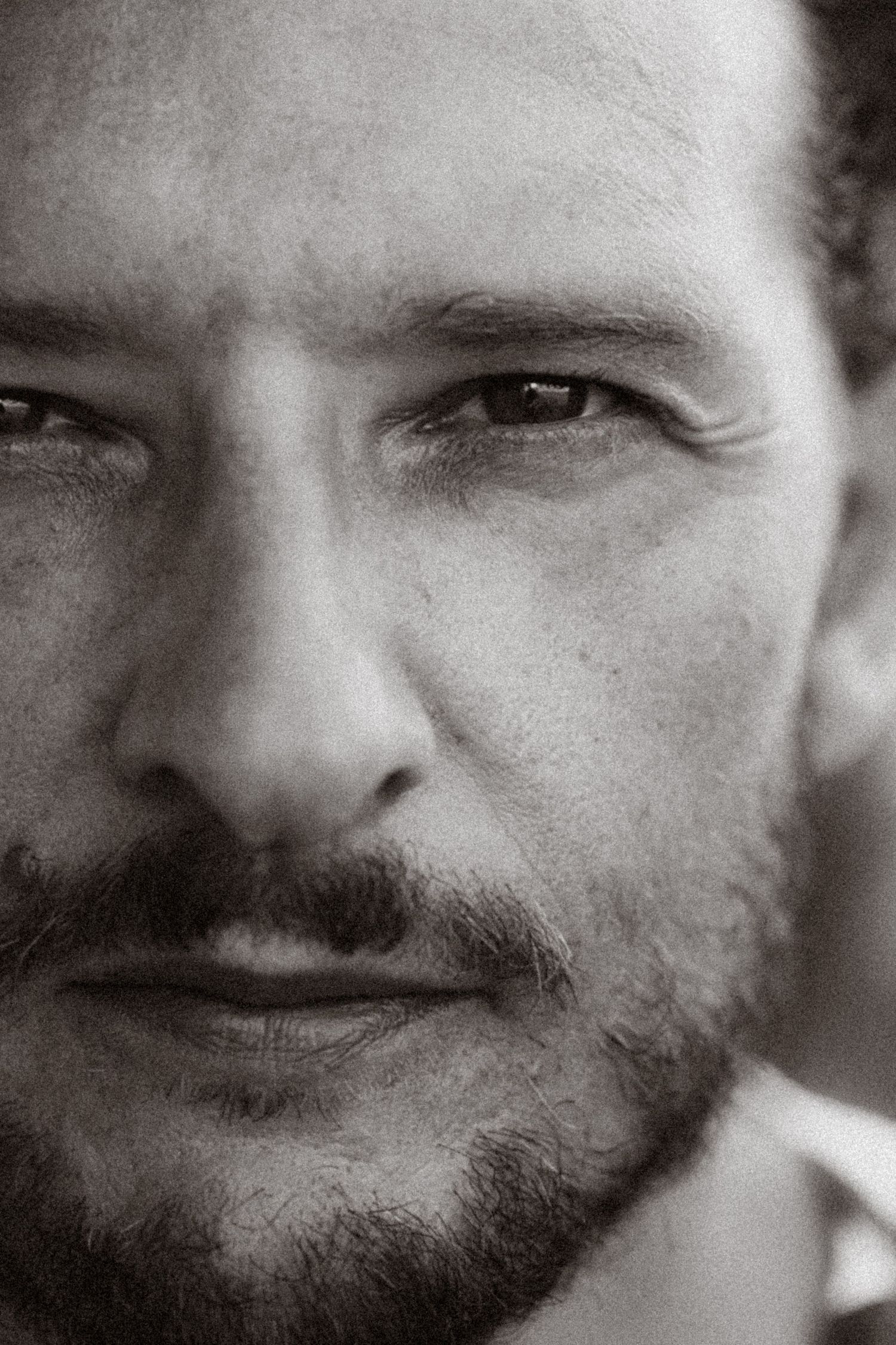 Close-up black and white portrait of a bearded man with intense eyes and stubble, captured in dramatic detail.