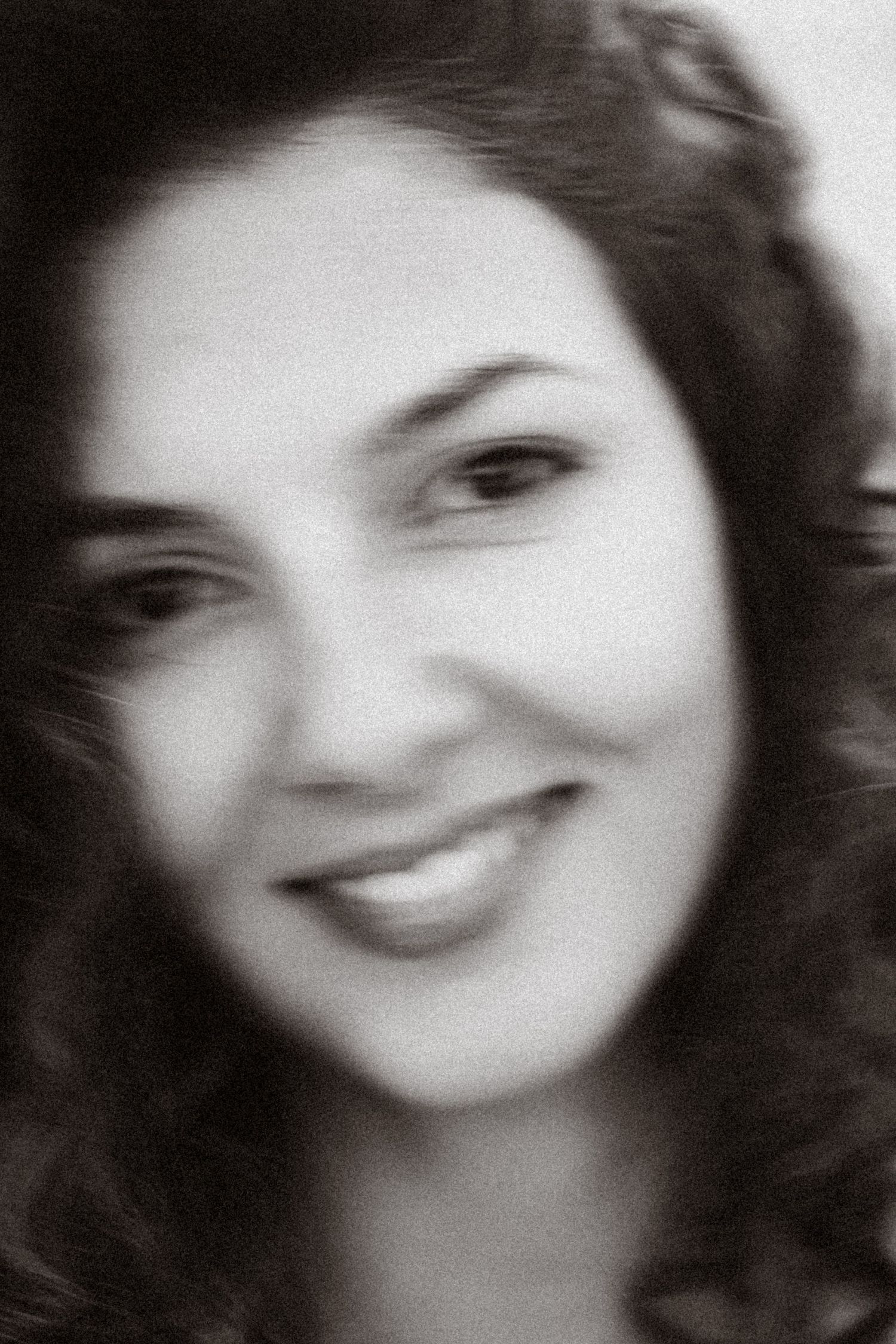 Black and white portrait of a smiling young woman with curly dark hair, soft focus photography style.