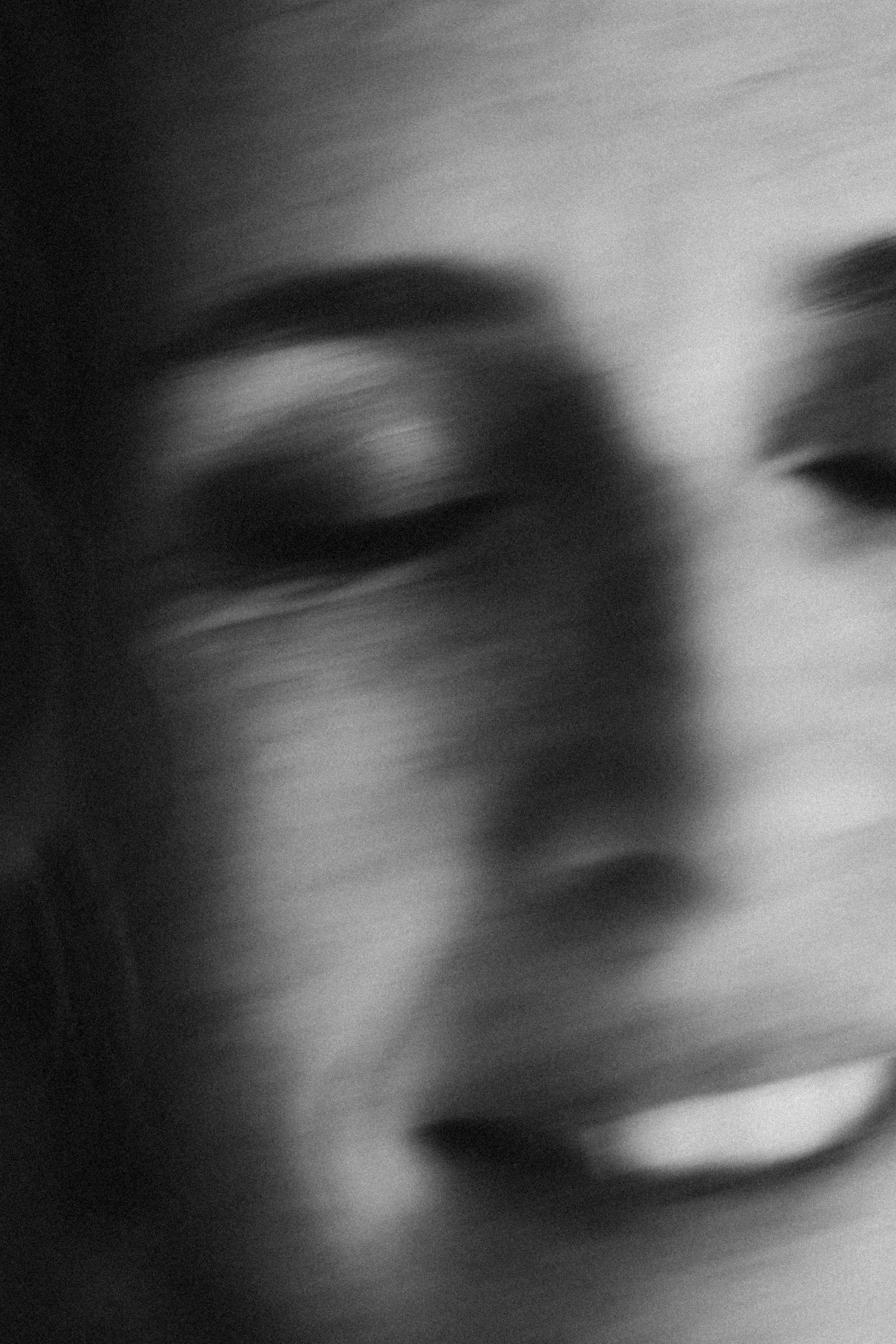 Black and white motion blur portrait of a woman smiling with eyes closed, artistic photography effect.