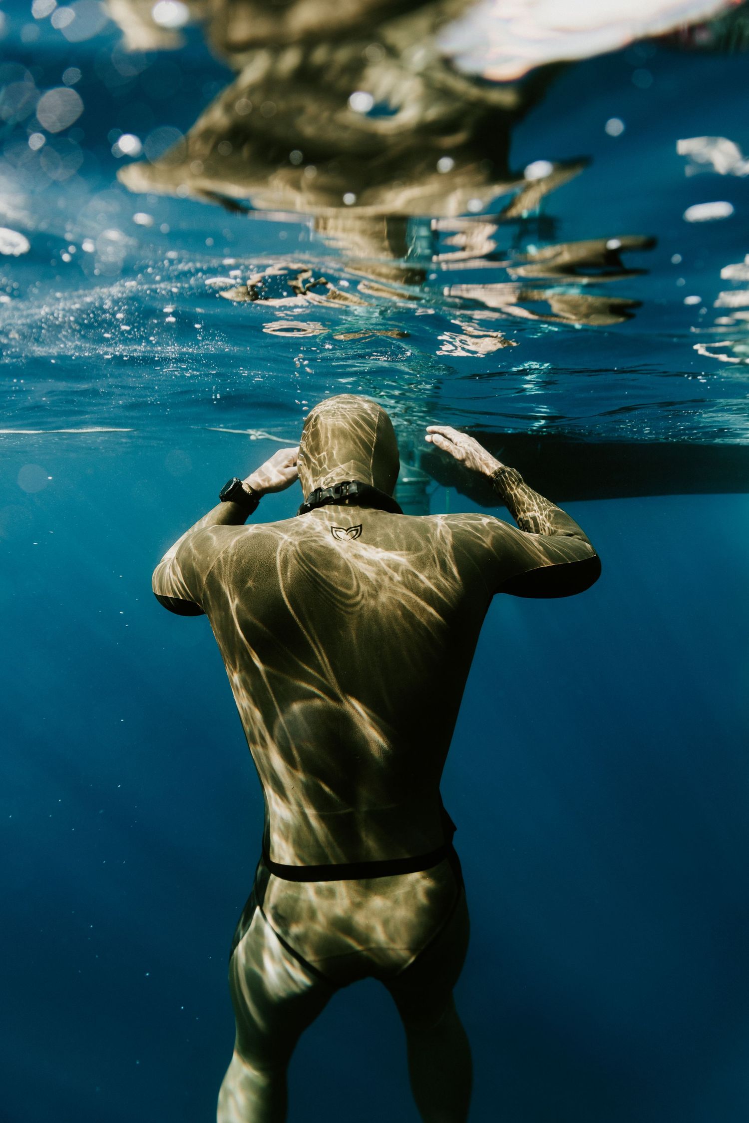 Underwater view of a person floating in a wetsuit with sunlight filtering through the surface.