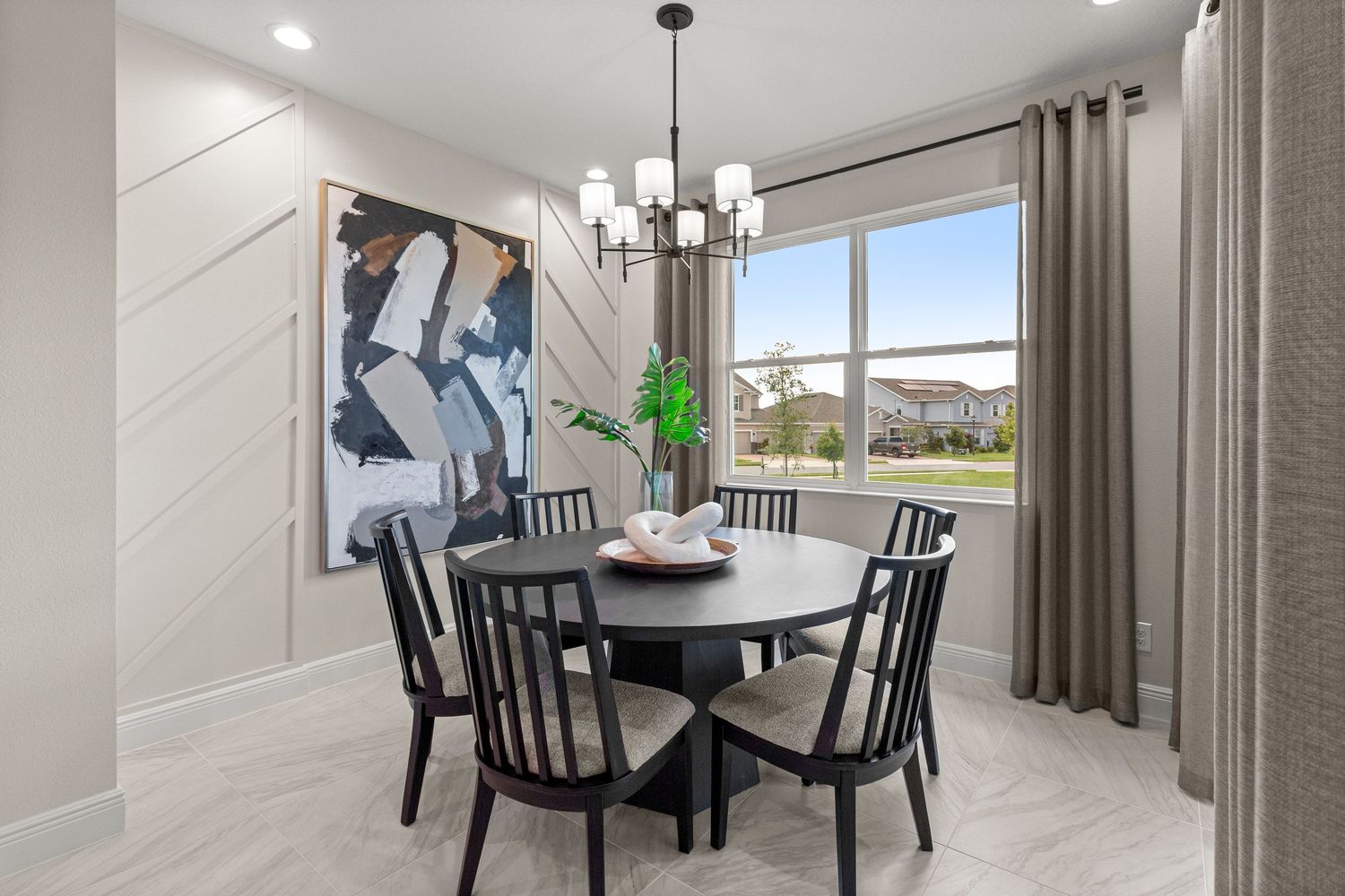 Bright dining room interior with modern table, chandelier lighting, and large window, professionally captured for real estate listing media.