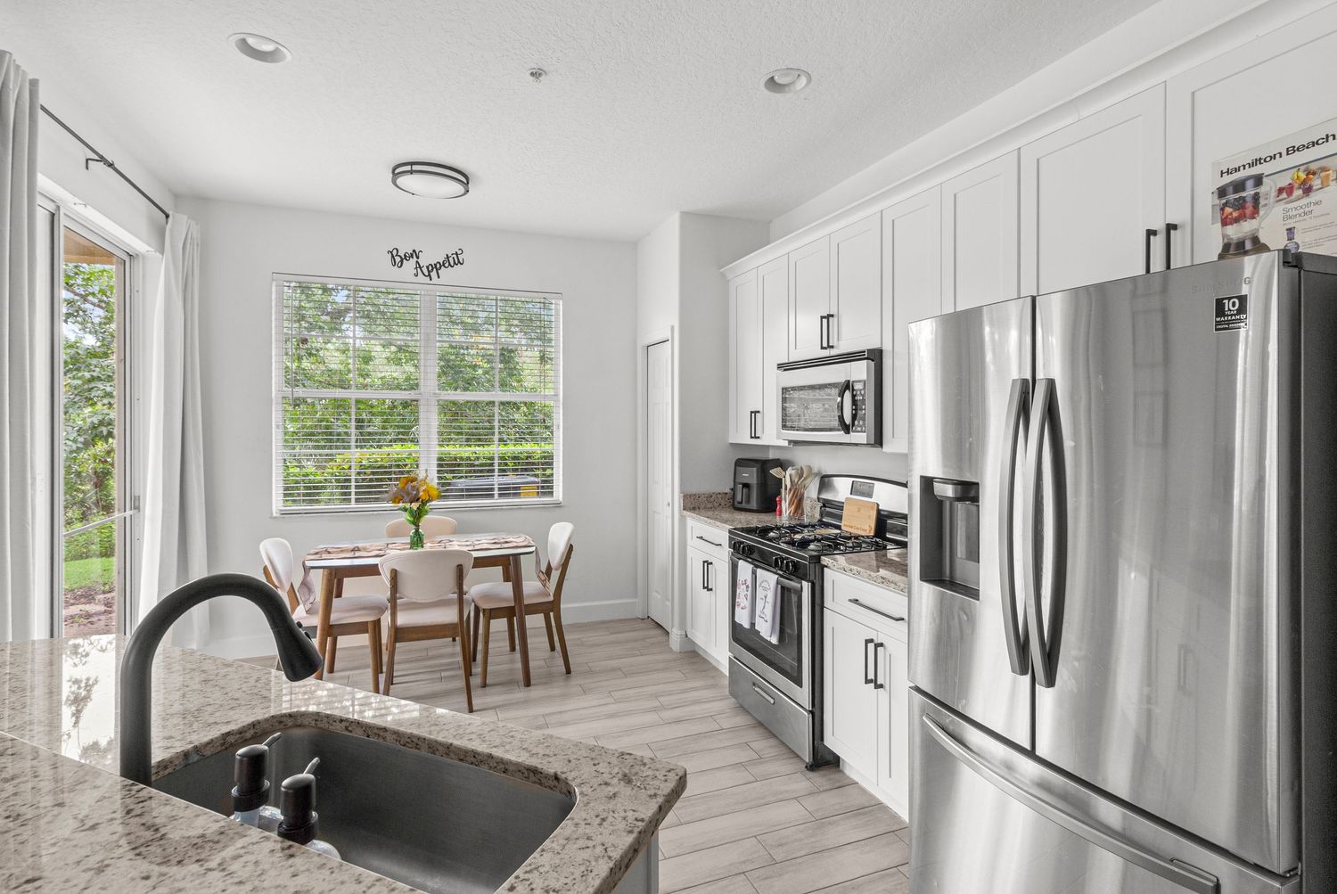 Bright modern kitchen in Tampa Florida featuring white cabinetry, stainless steel appliances, large island with farmhouse sink, and open-con