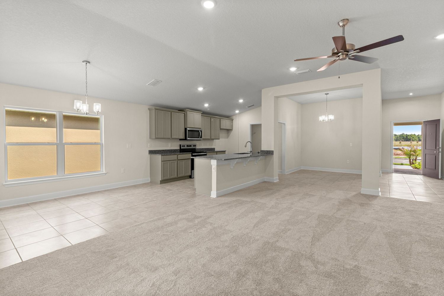 Open living area with kitchen, tile flooring, and ceiling fan in modern Florida home