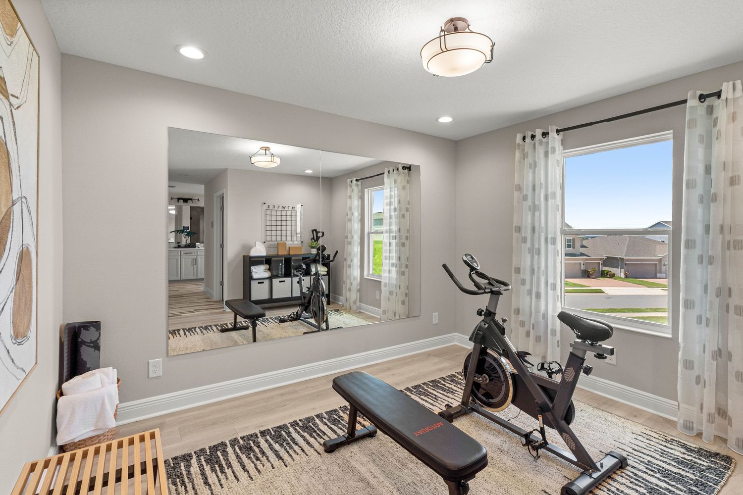 Well-equipped Kissimmee Florida home gym with exercise equipment, wood flooring, large windows, and bright natural lighting. Professional.