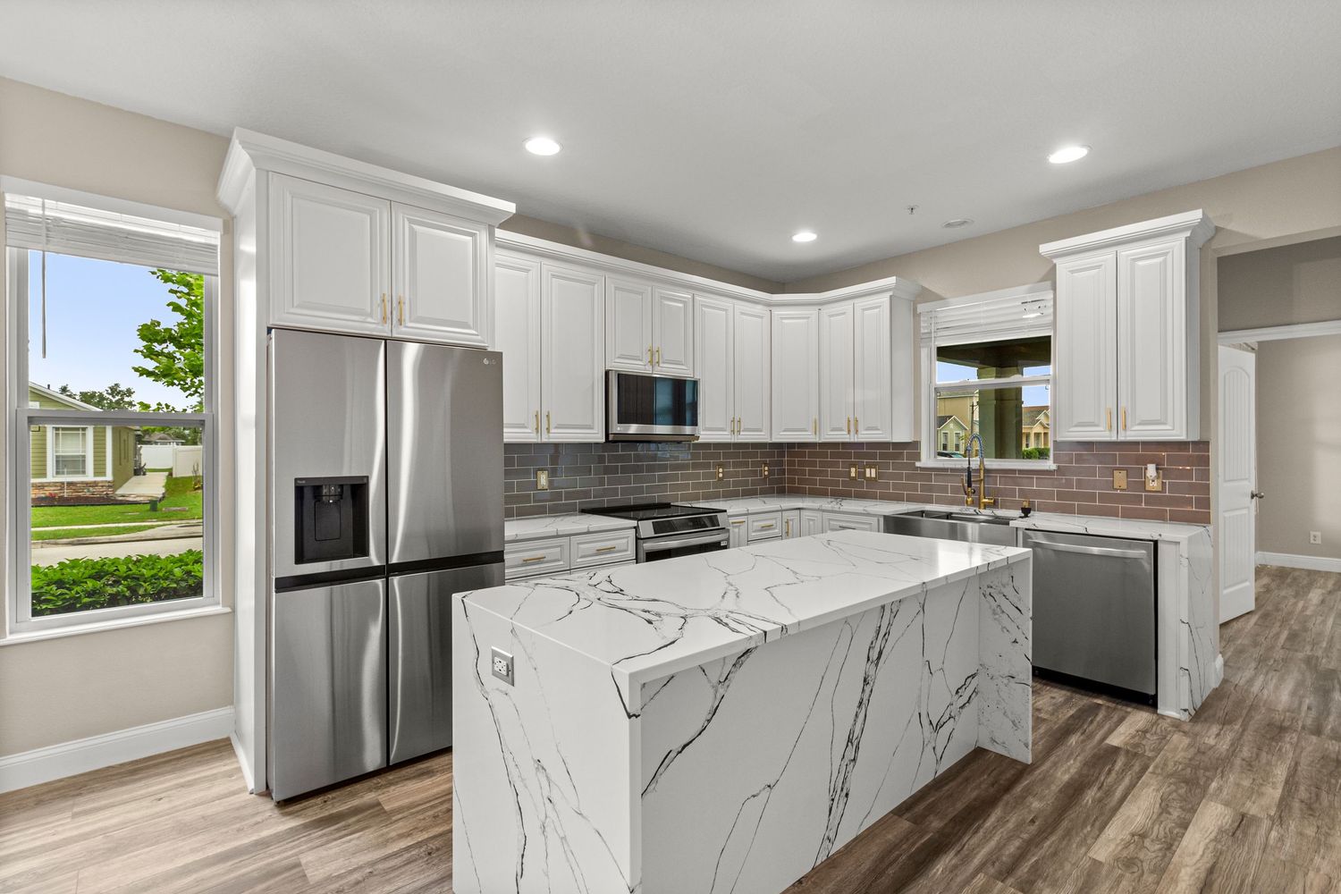 Modern kitchen real estate photo with white cabinets, stainless appliances, marble-style island, and bright lighting.