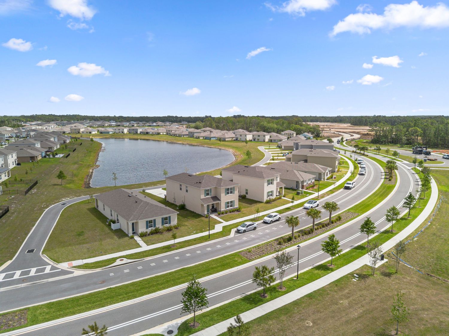 Wide aerial shot of neighborhood with lake, roads, and homes under blue sky