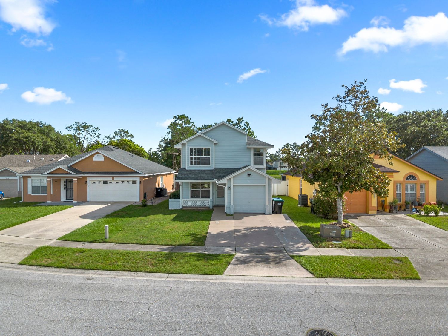Elevated street view of a two-story suburban home with a two-car garage, driveway, green lawn, and clear blue sky.