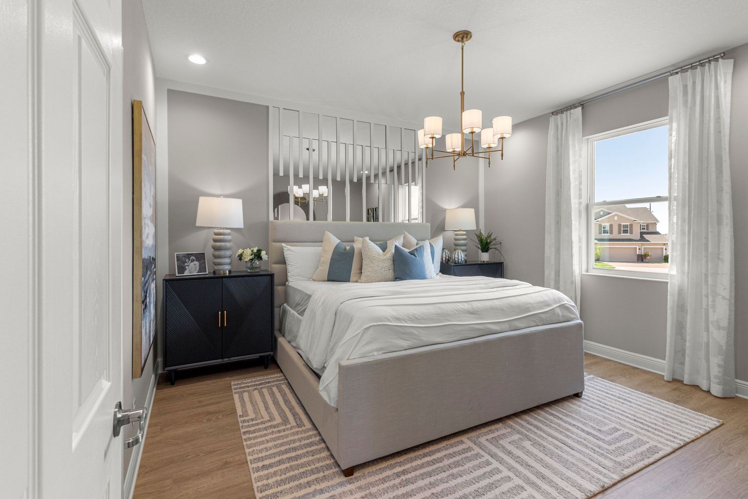 Modern Clermont Florida bedroom featuring elegant chandelier, white bedding, dark furniture, and wood-look flooring. Real estate