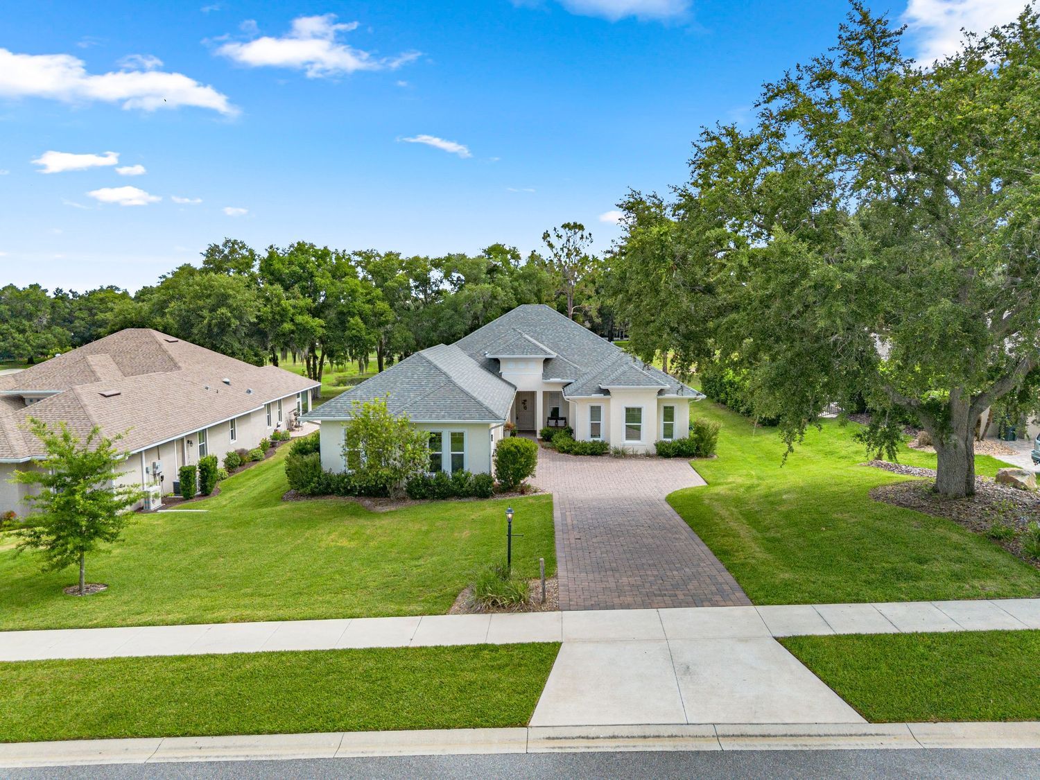 Drone exterior photo showing the home’s front yard, driveway, roofline, and surrounding green landscaping.