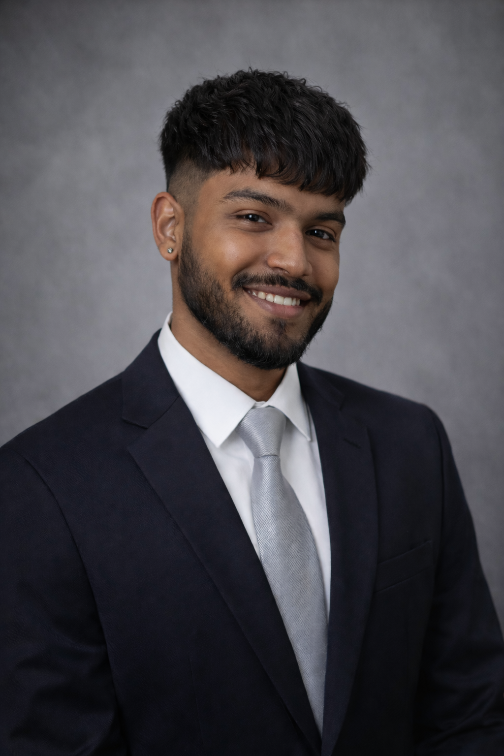 Professional real estate headshot of a well-dressed agent in navy suit with groomed beard, modern hairstyle, and confident smile.