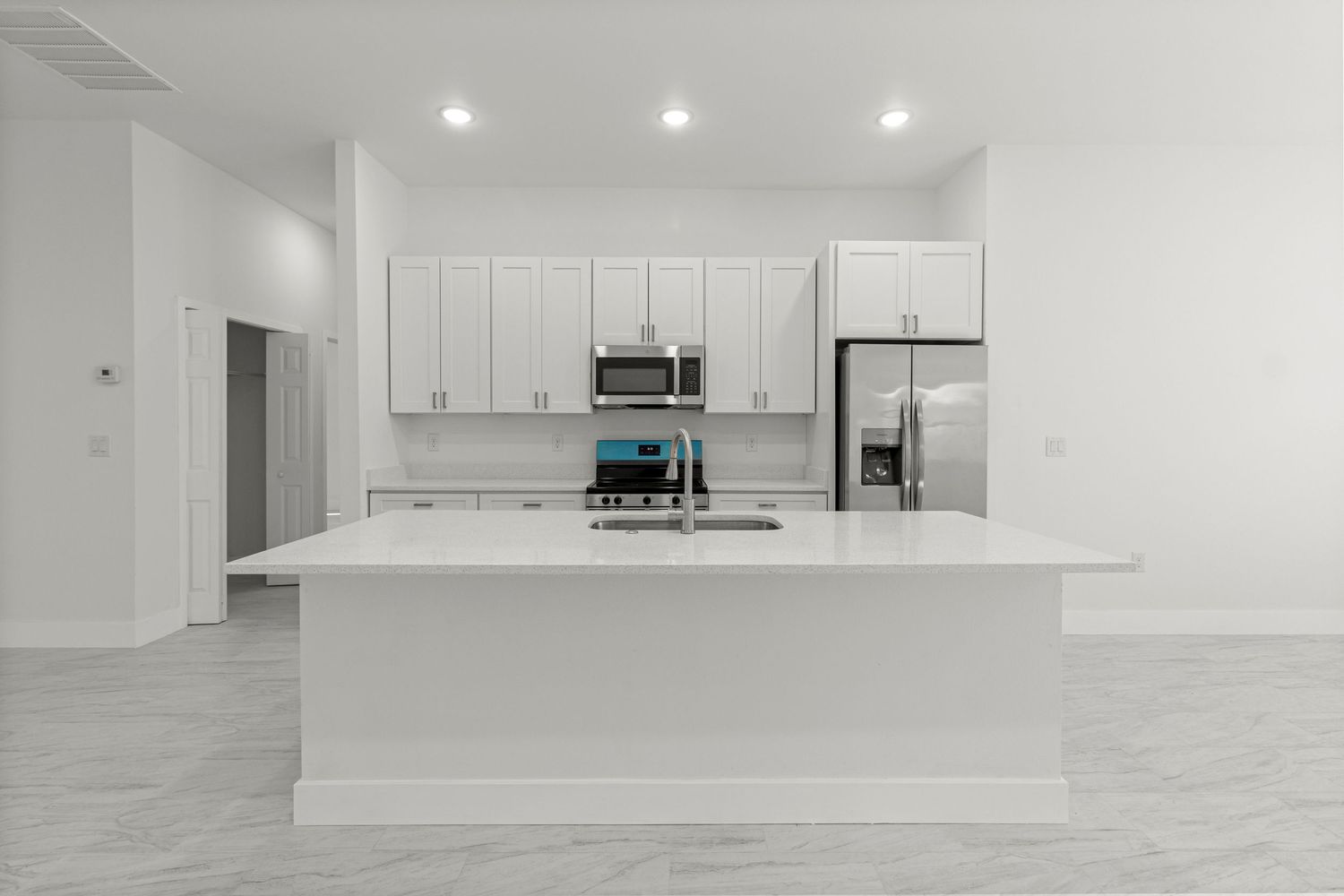 Bright modern Ocala Florida kitchen interior featuring white cabinetry, large island, stainless appliances, and open layout. Professional.