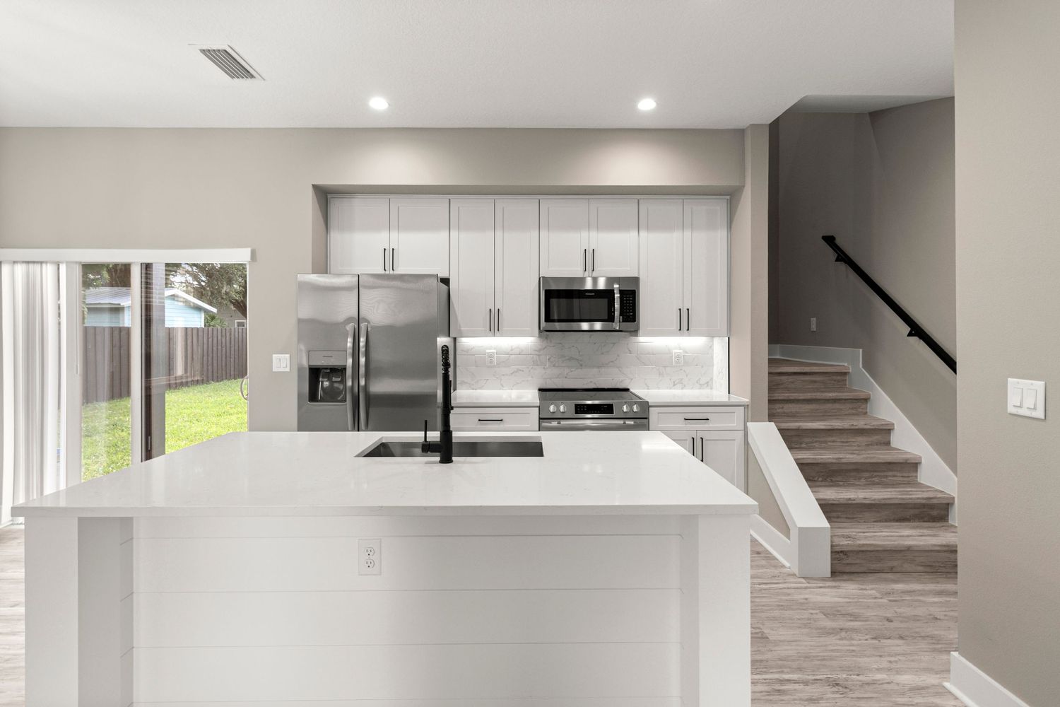 Contemporary Orlando Florida kitchen interior featuring white cabinets, modern island, stainless appliances, and open staircase design.