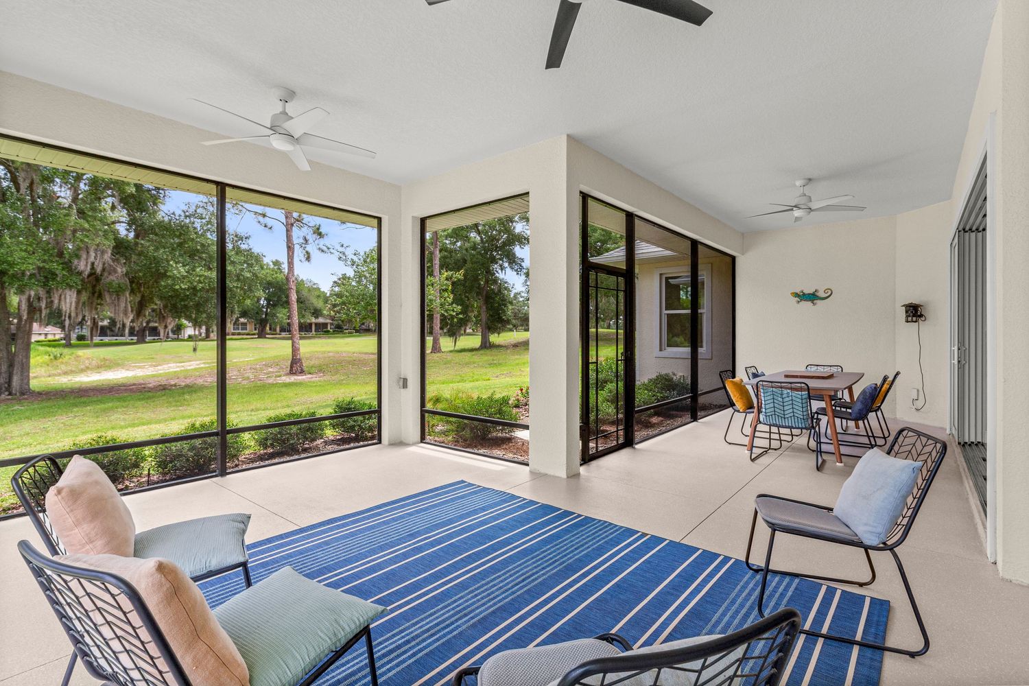 Covered patio real estate photo with seating area, sliding glass doors, ceiling fans, and peaceful outdoor views.