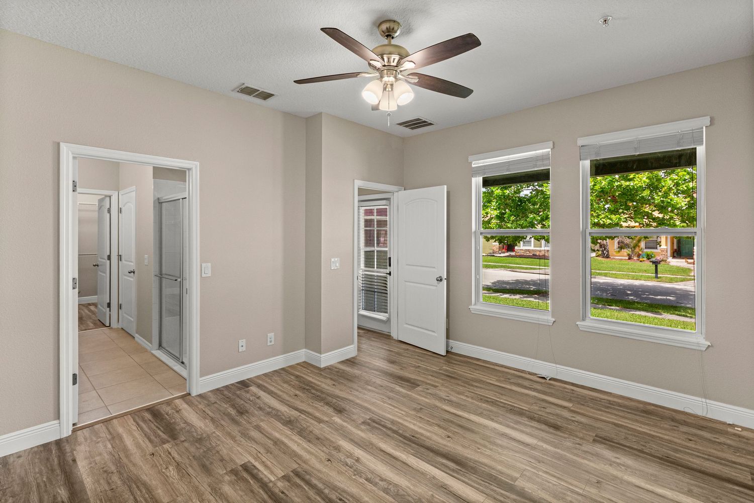 Open living room real estate photo with neutral walls, ceiling fan, large windows, and clean modern flooring.