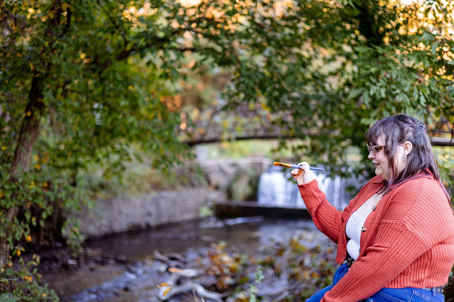 A Senior artist who enjoys painting during her senior session near a waterfall in the Ozarks