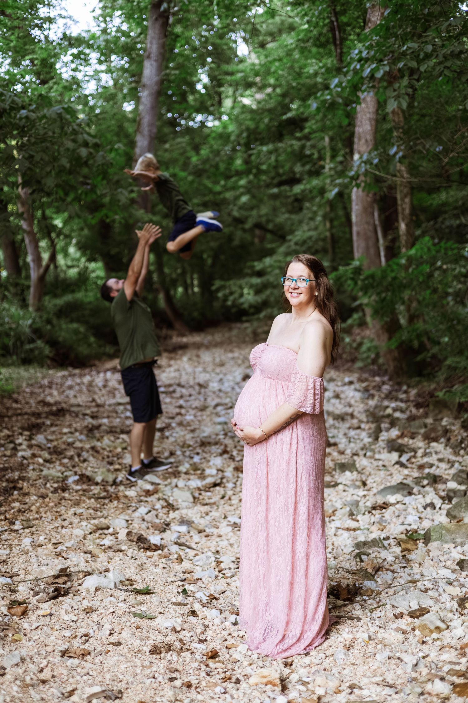 Maternity sessions in Reed Springs MO with dad throwing oldest sun in the air in a creek bed with Refined by Fire Photography