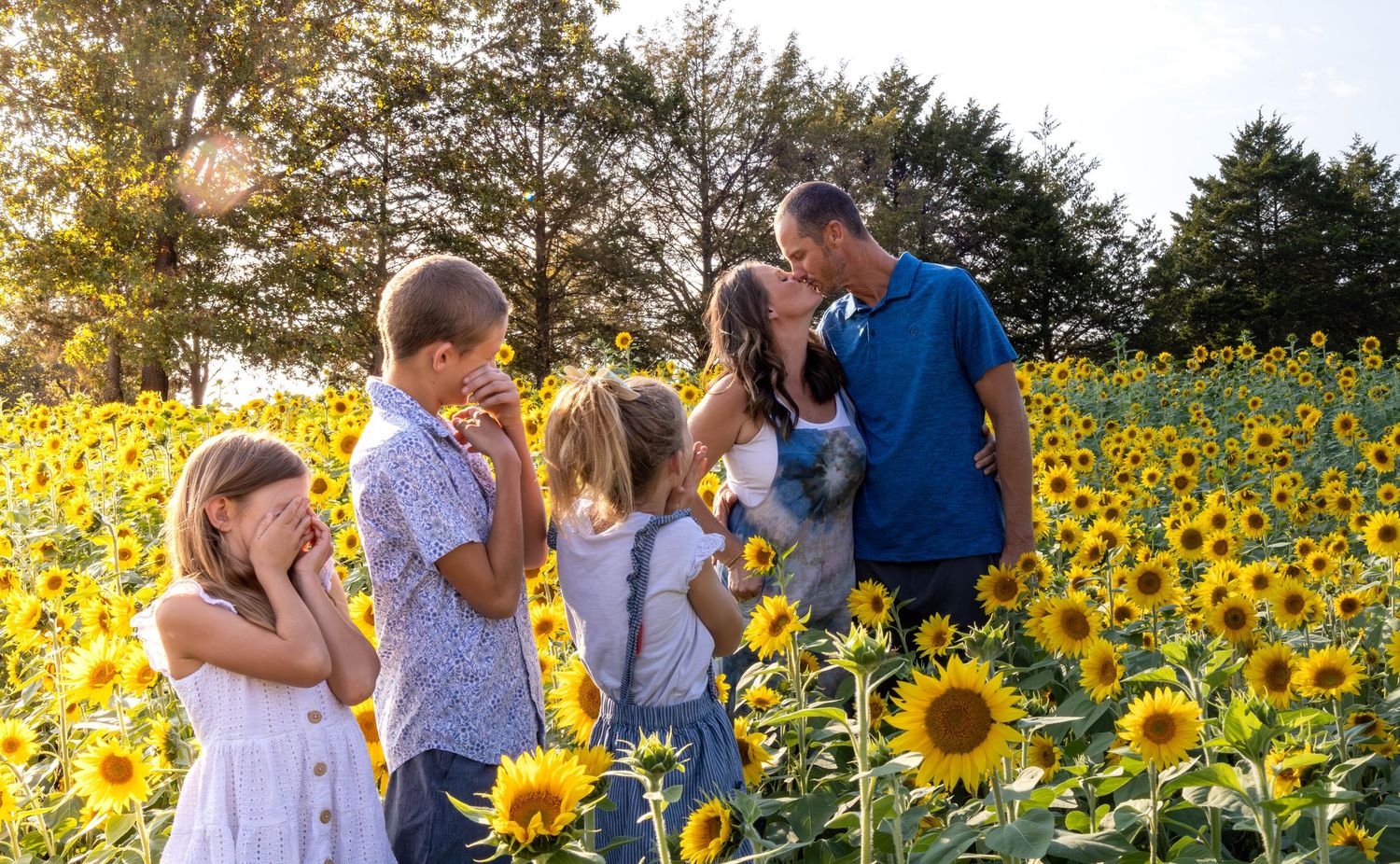 mom and dad kissing in a sunflower field while the kids turn their heads in Marshfield MO during a session with Refined by FIre Photogaphy.