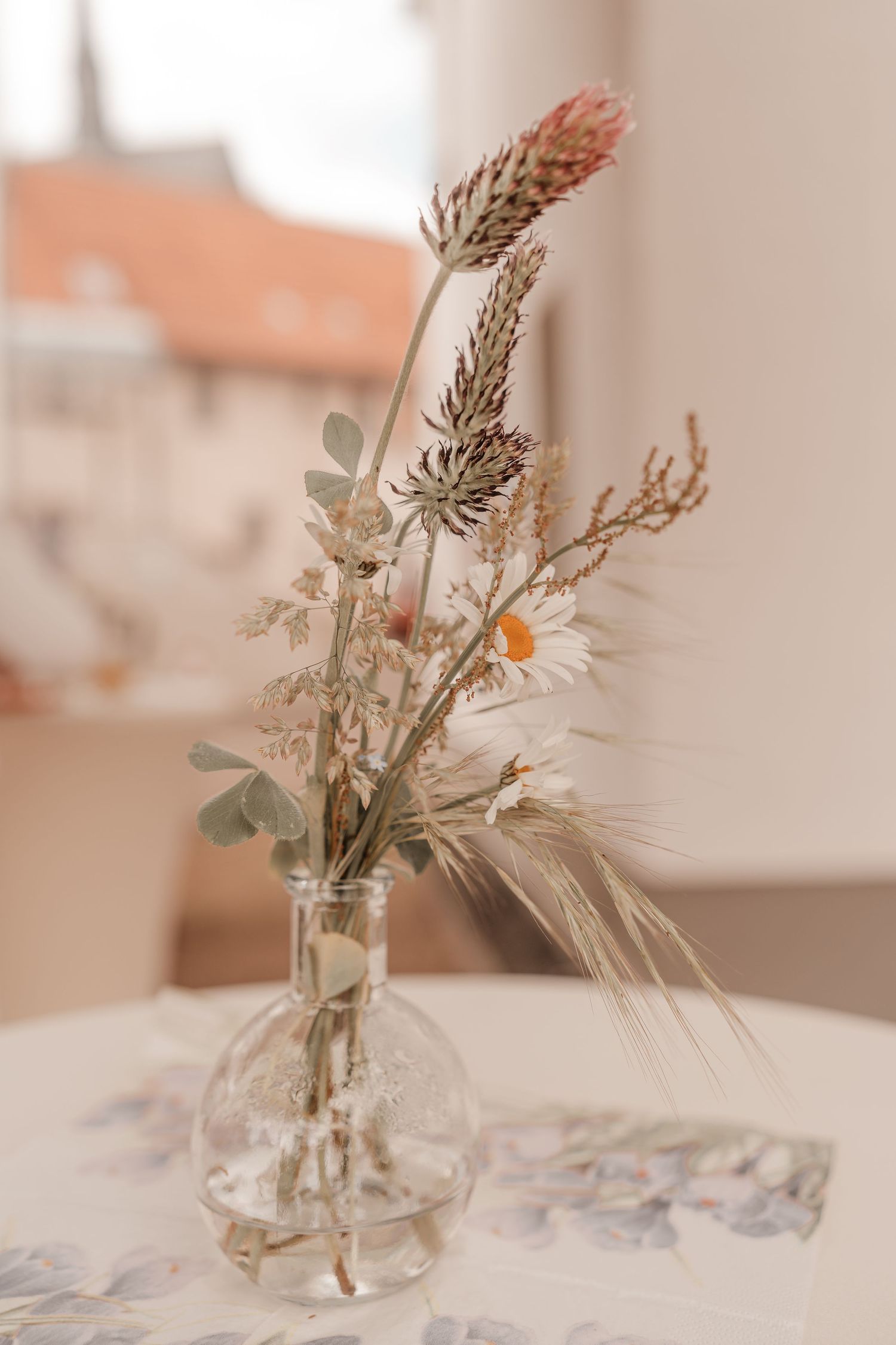 Minimalist dried flower arrangement in clear glass vase on white tablecloth.