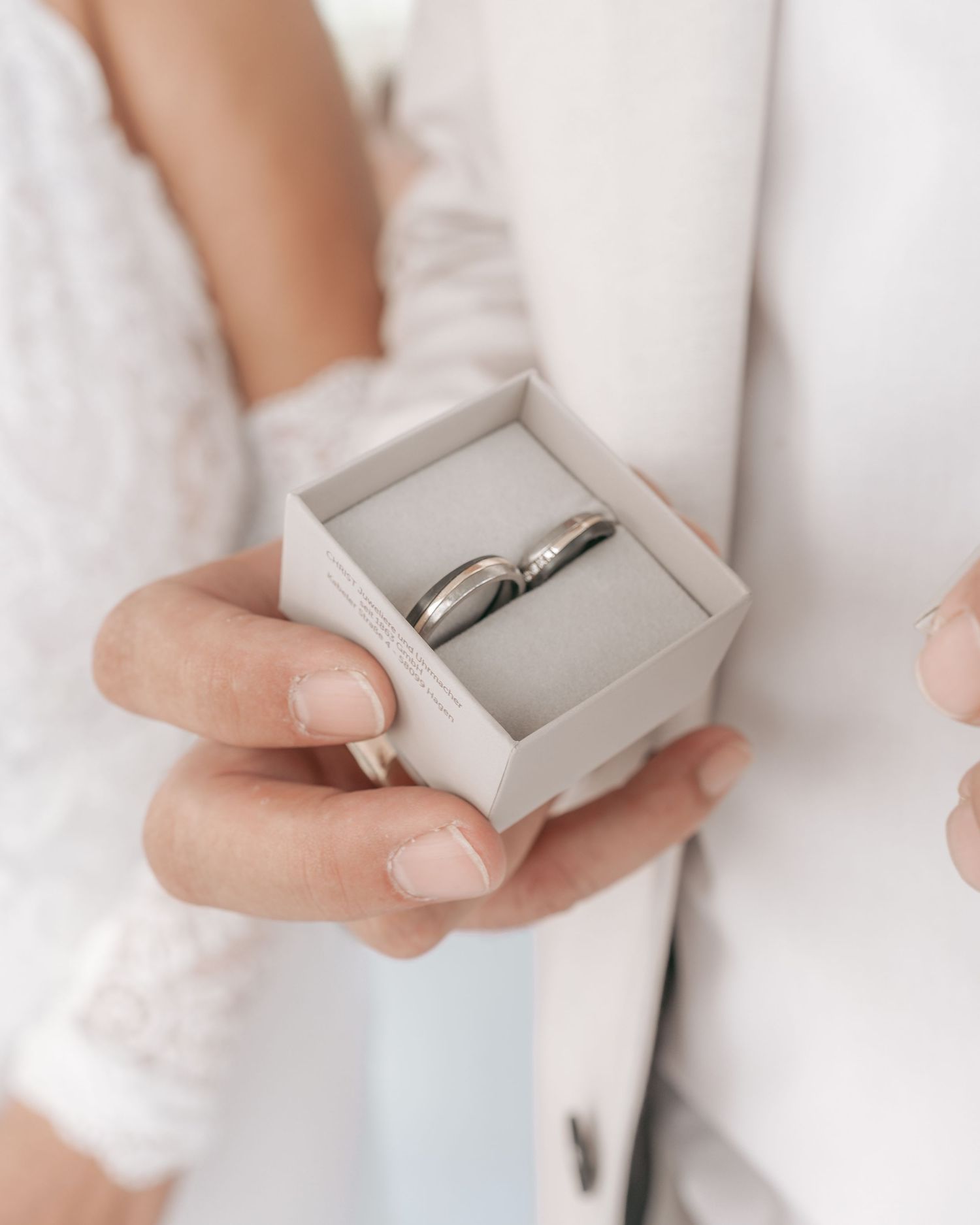 Hands holding small gray ring box containing engagement ring.