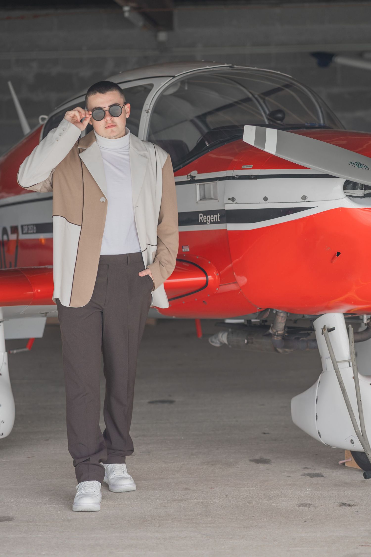 Stylish person posing next to a red and white private aircraft in a hangar.