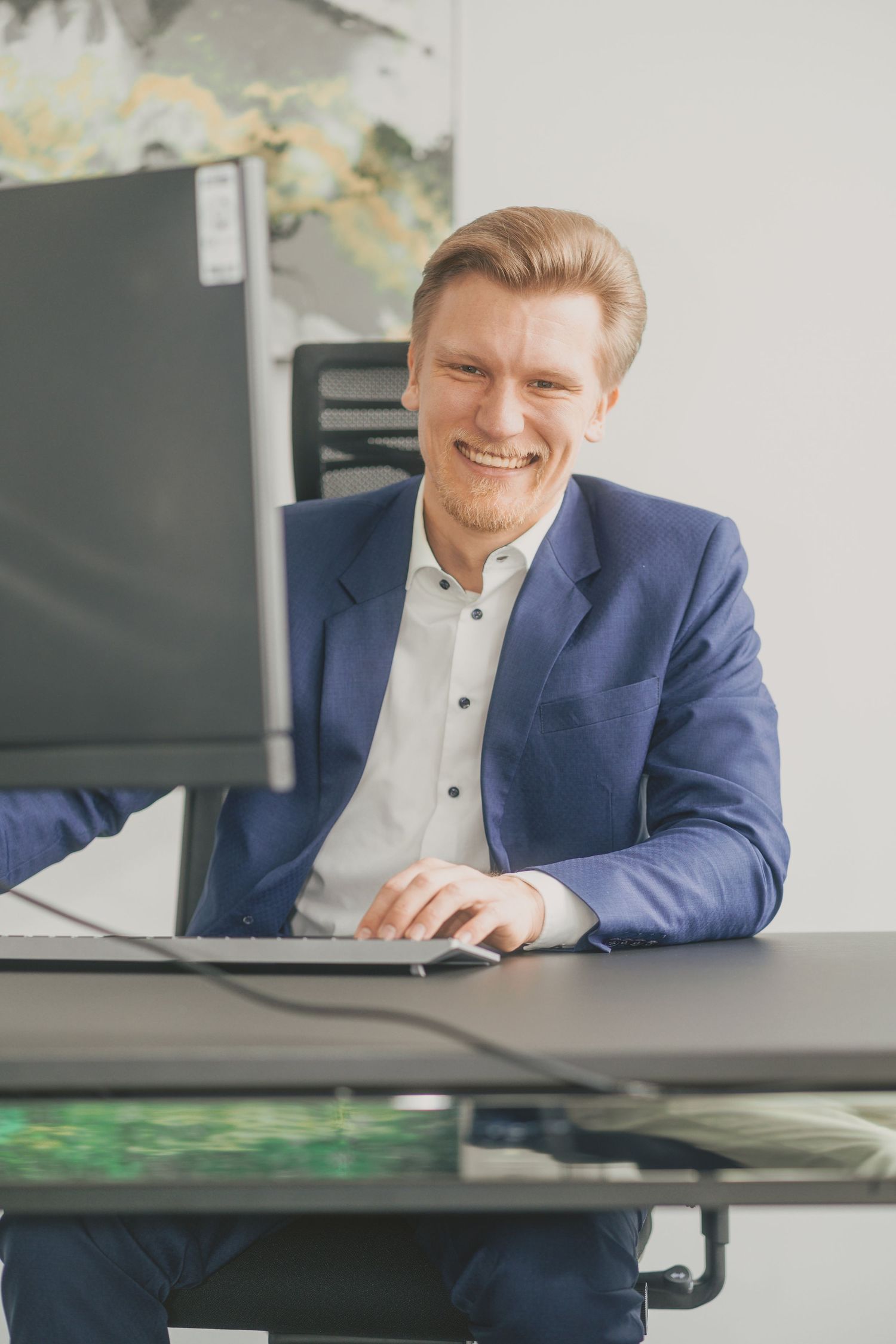 Professional sitting at desk with computer monitors in modern office setting.