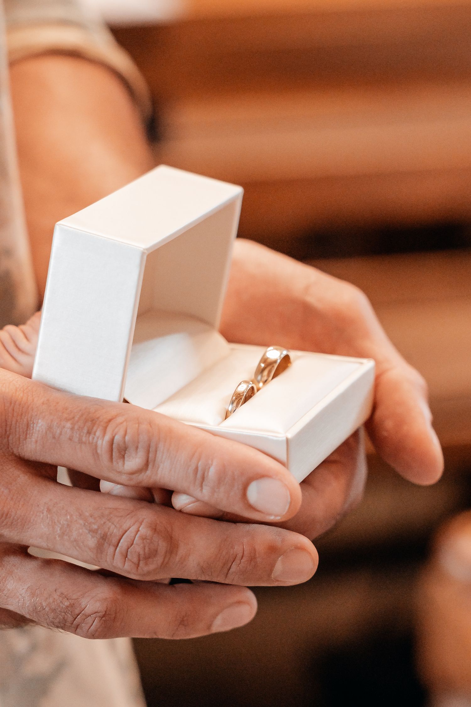 Elderly hands holding an open white jewelry box with a gold wedding ring inside.