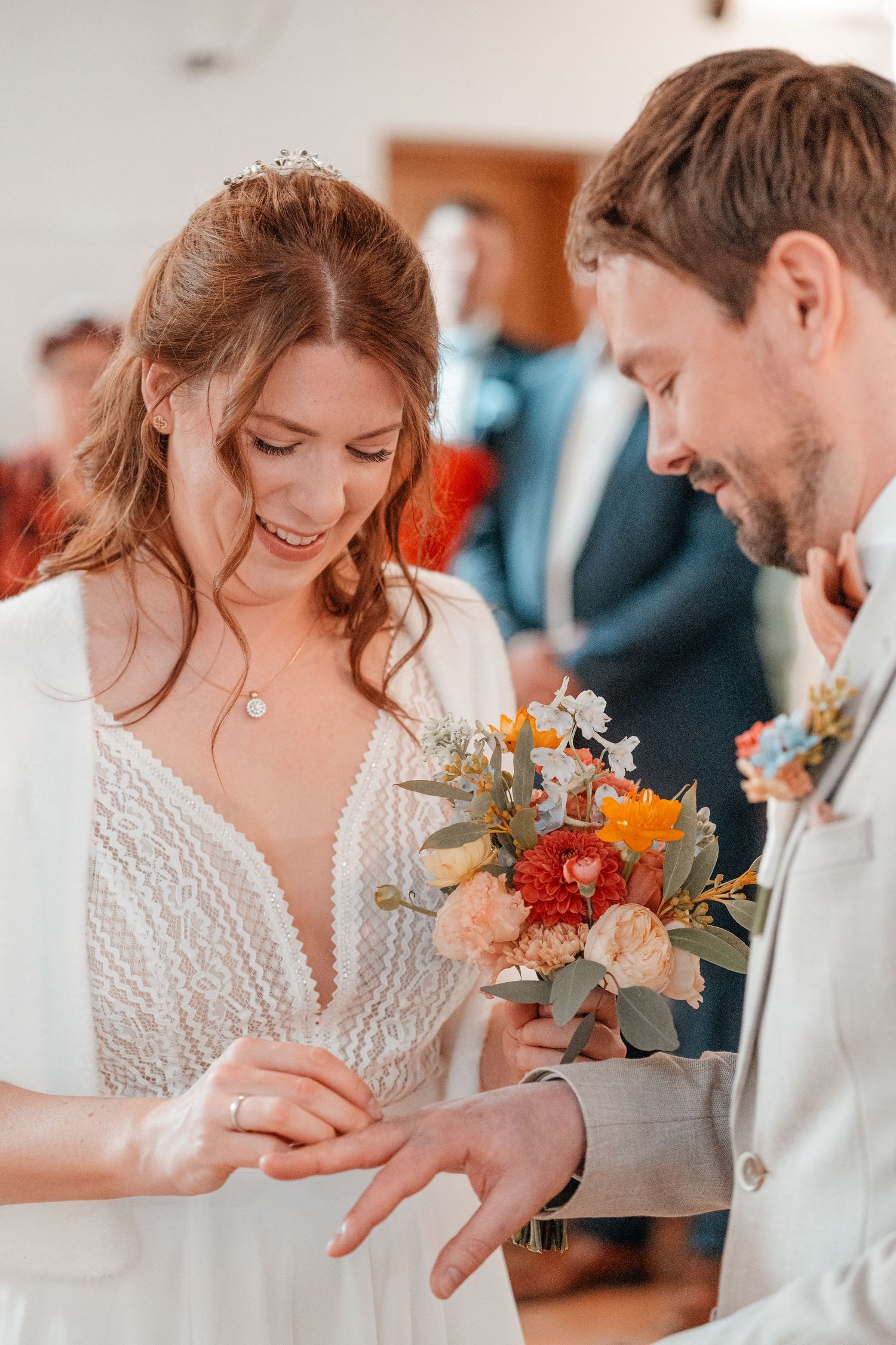 Wedding ceremony moment showing exchange of rings with coral and peach floral bouquet.