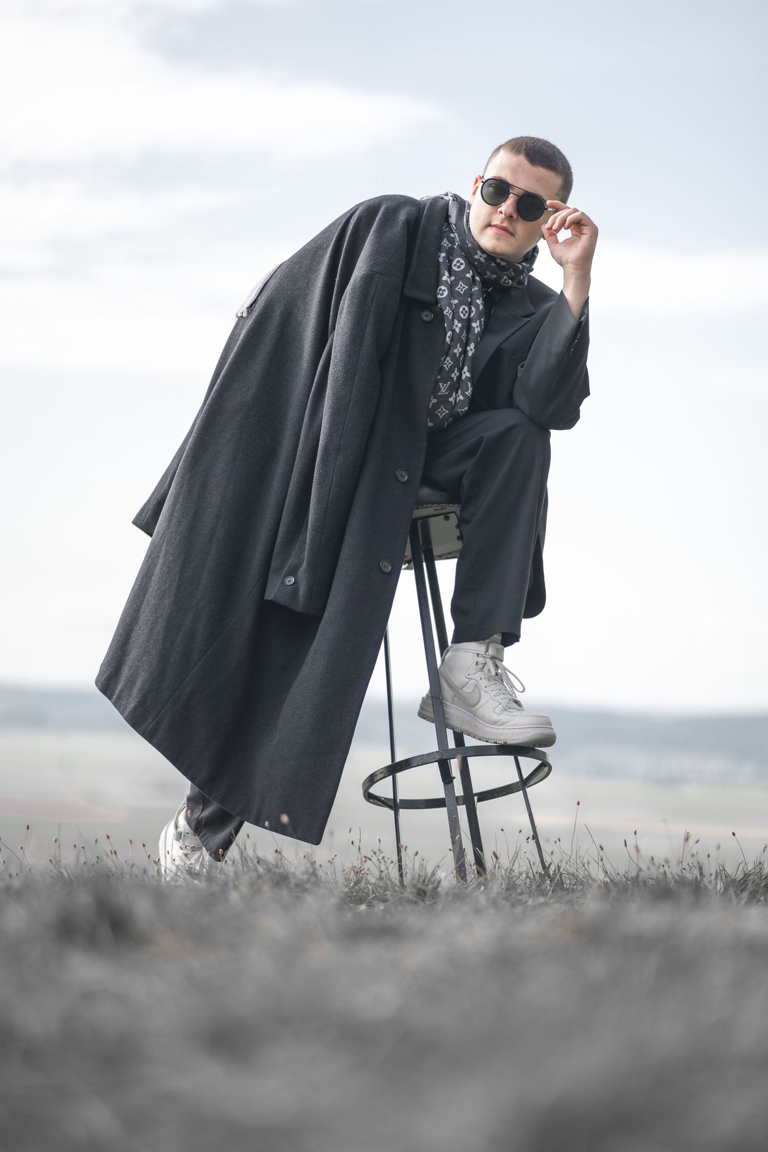 Dramatic portrait of someone in a long coat sitting on a stool against a misty backdrop.