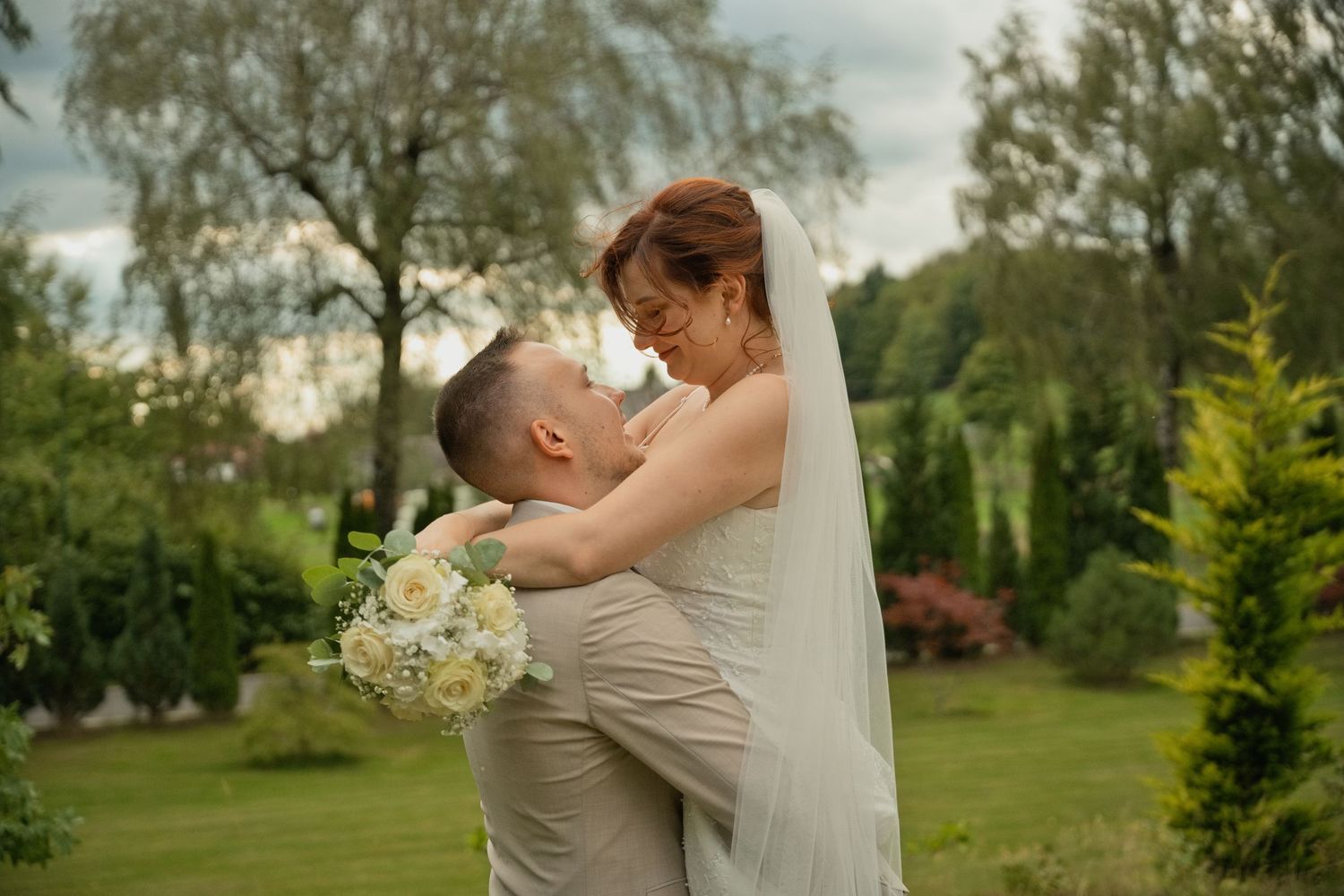 Bride and groom sharing a romantic moment in a lush green garden, with the bride holding a white bouquet.