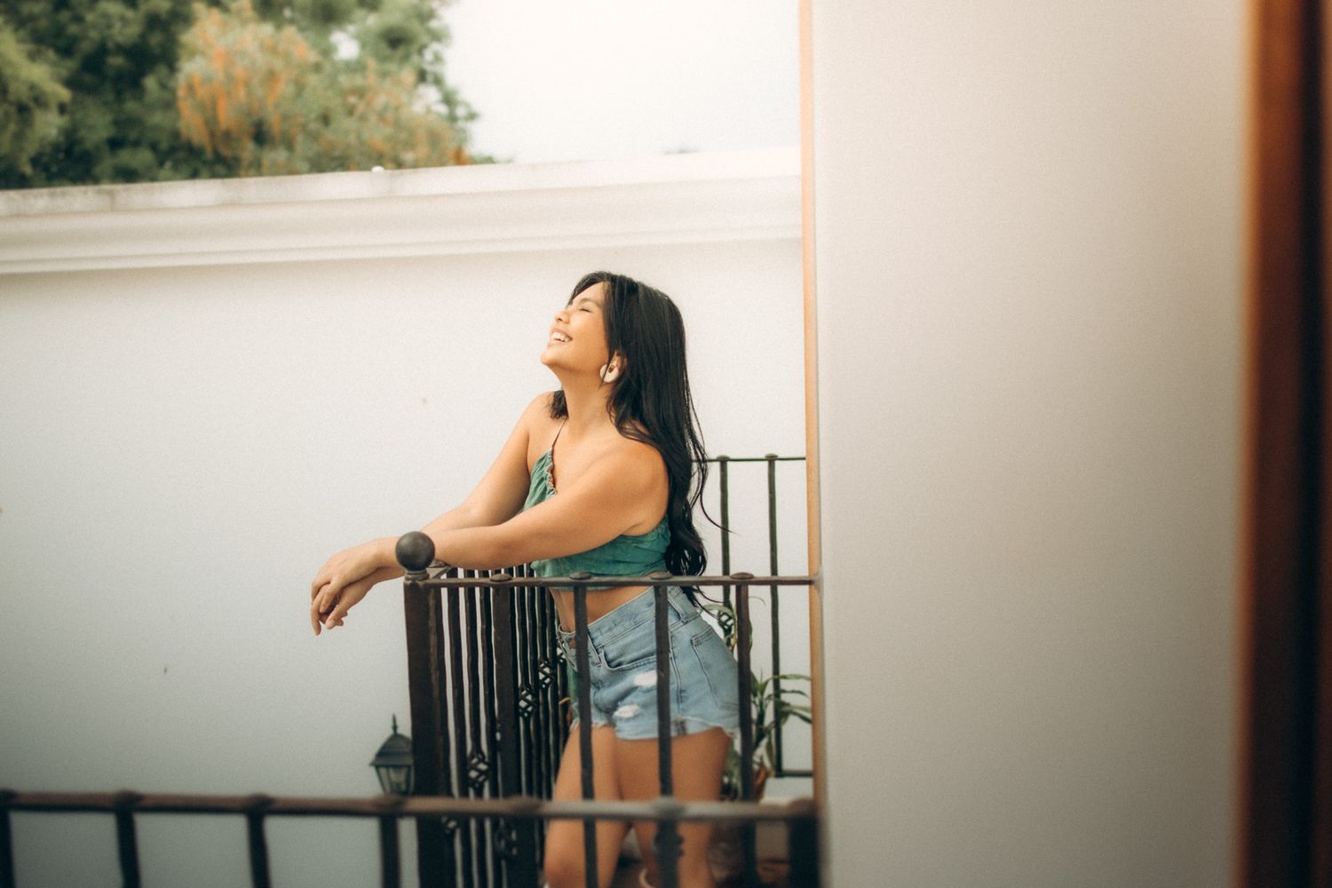 Person in denim shorts leans against balcony railing at sunset with dreamy warm lighting and soft focus.