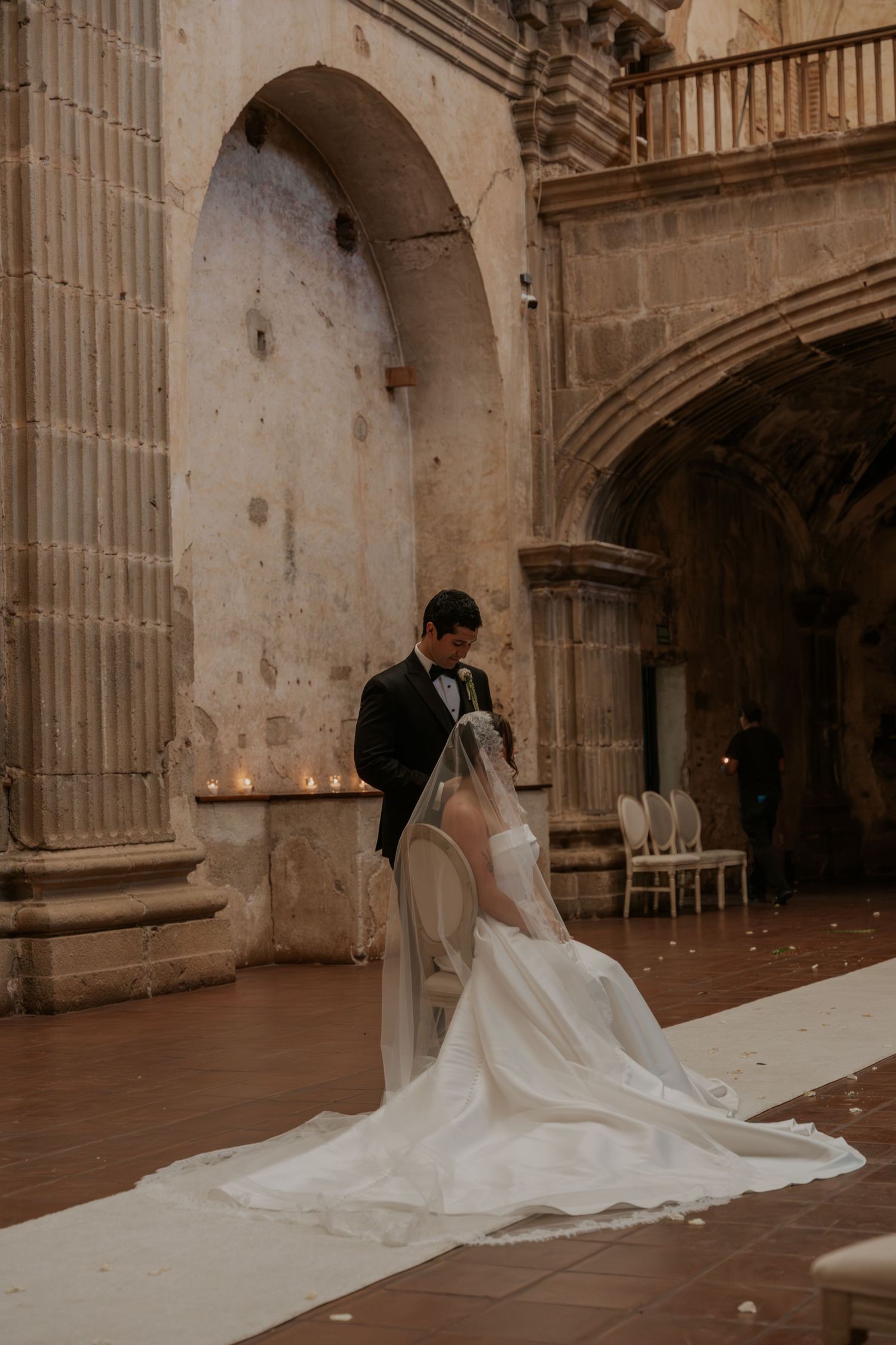 Bride and groom share an intimate moment in a stunning stone archway venue, with a flowing white cathedral veil.