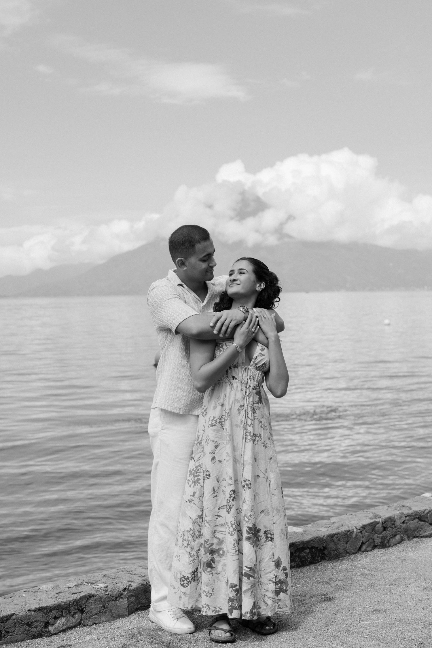 A romantic couple in white attire shares tender moments by the ocean in a series of black and white photographs.