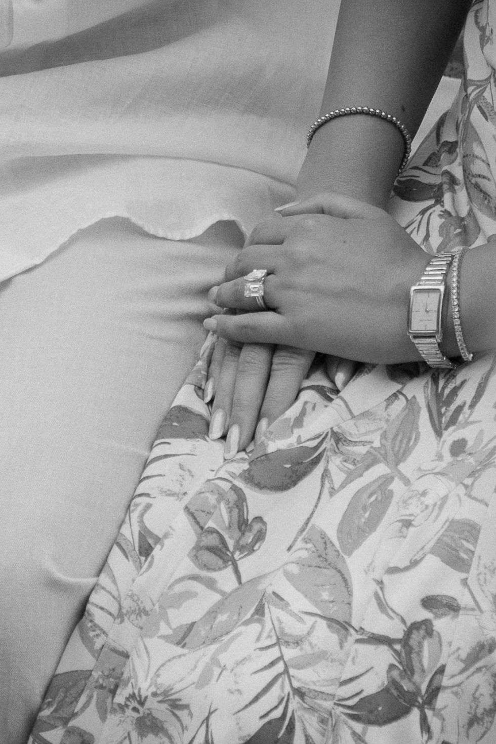 Close-up view of hands wearing rings and bracelets resting on a floral patterned fabric.