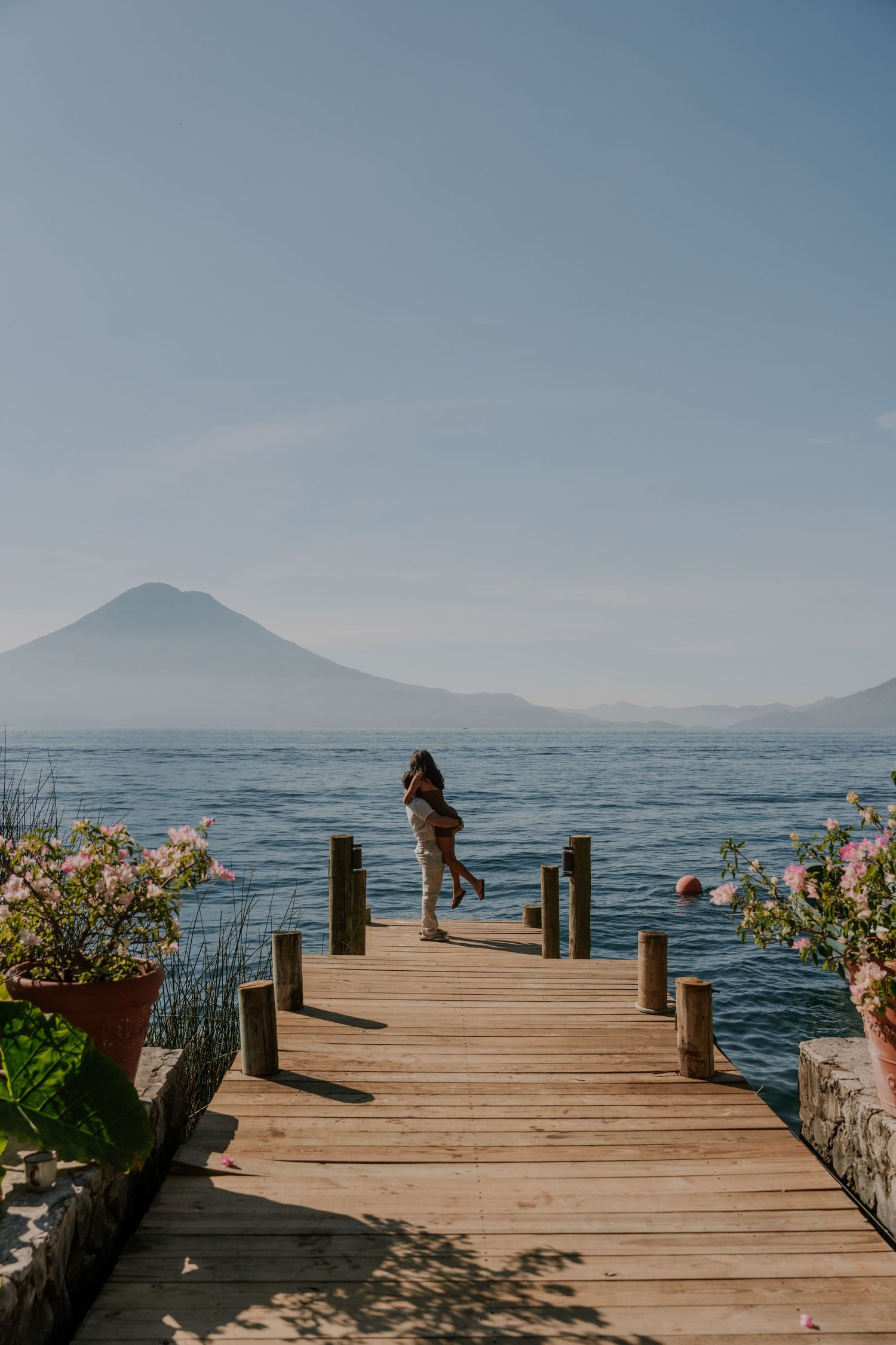 A wooden dock on Lake Atitlan in Guatemala with a silhouetted figure standing at the end and a volcano in the background.