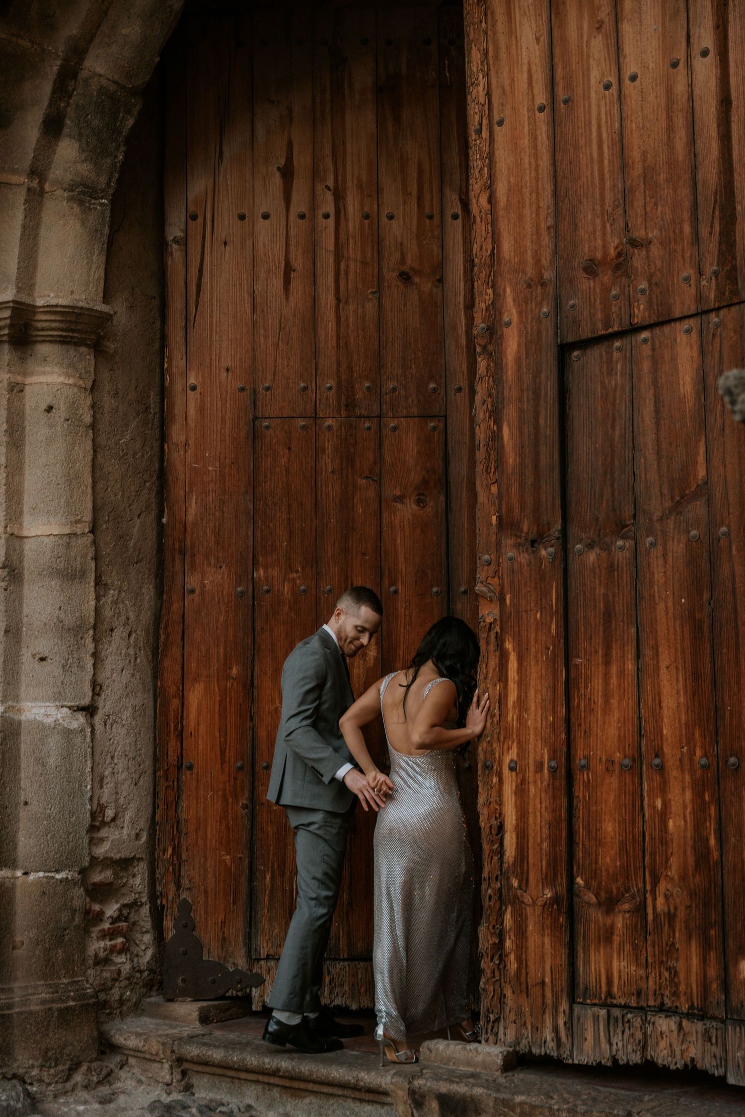 A romantic moment against a rustic wooden door in an old stone archway.