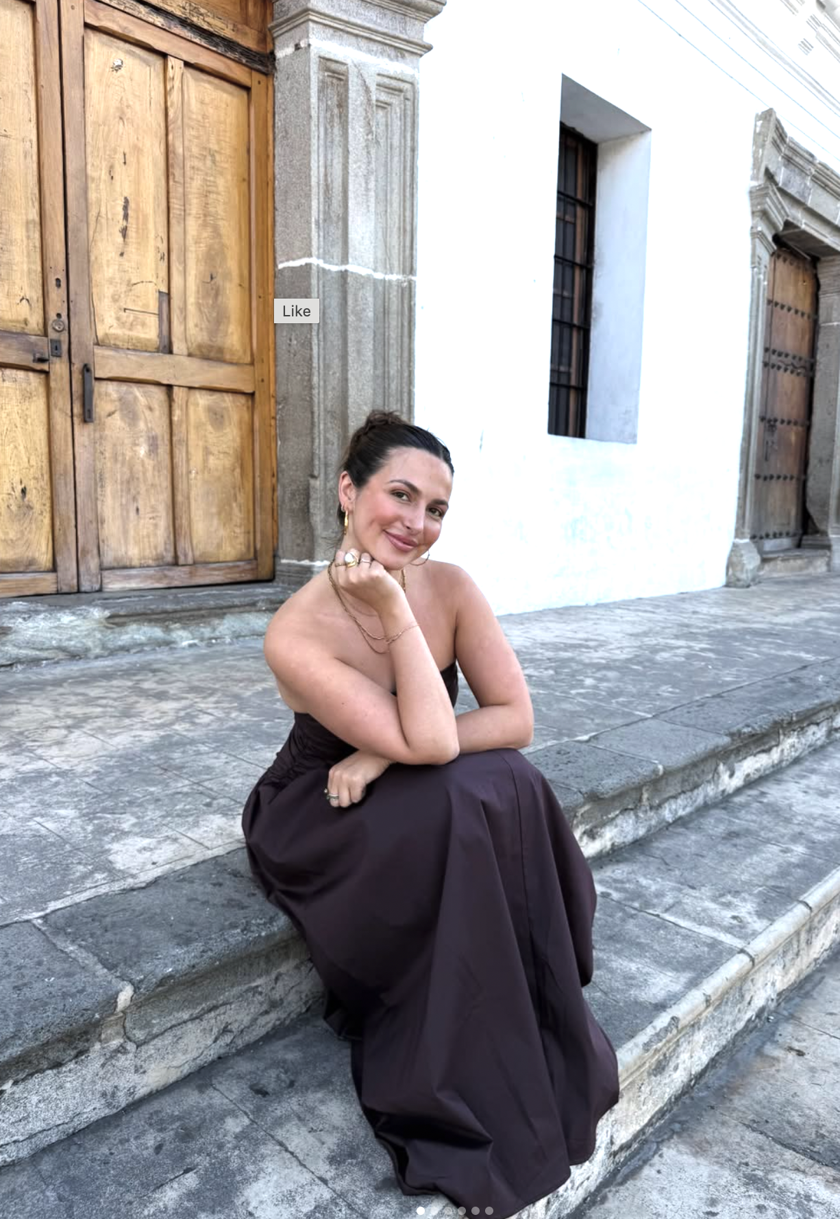 A person in a dark dress sits casually on stone steps outside historic wooden doors.