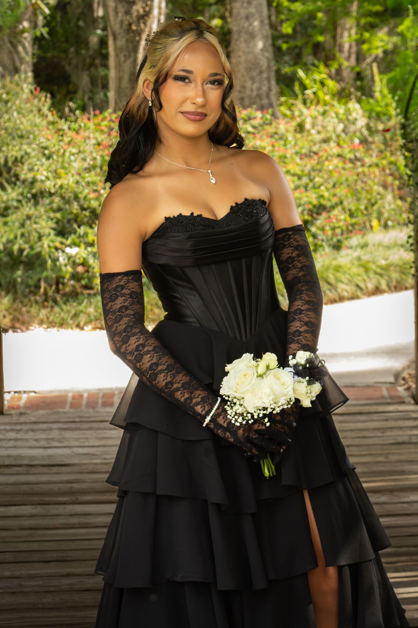 Young woman in black strapless tiered formal gown with lace gloves holding white bouquet.