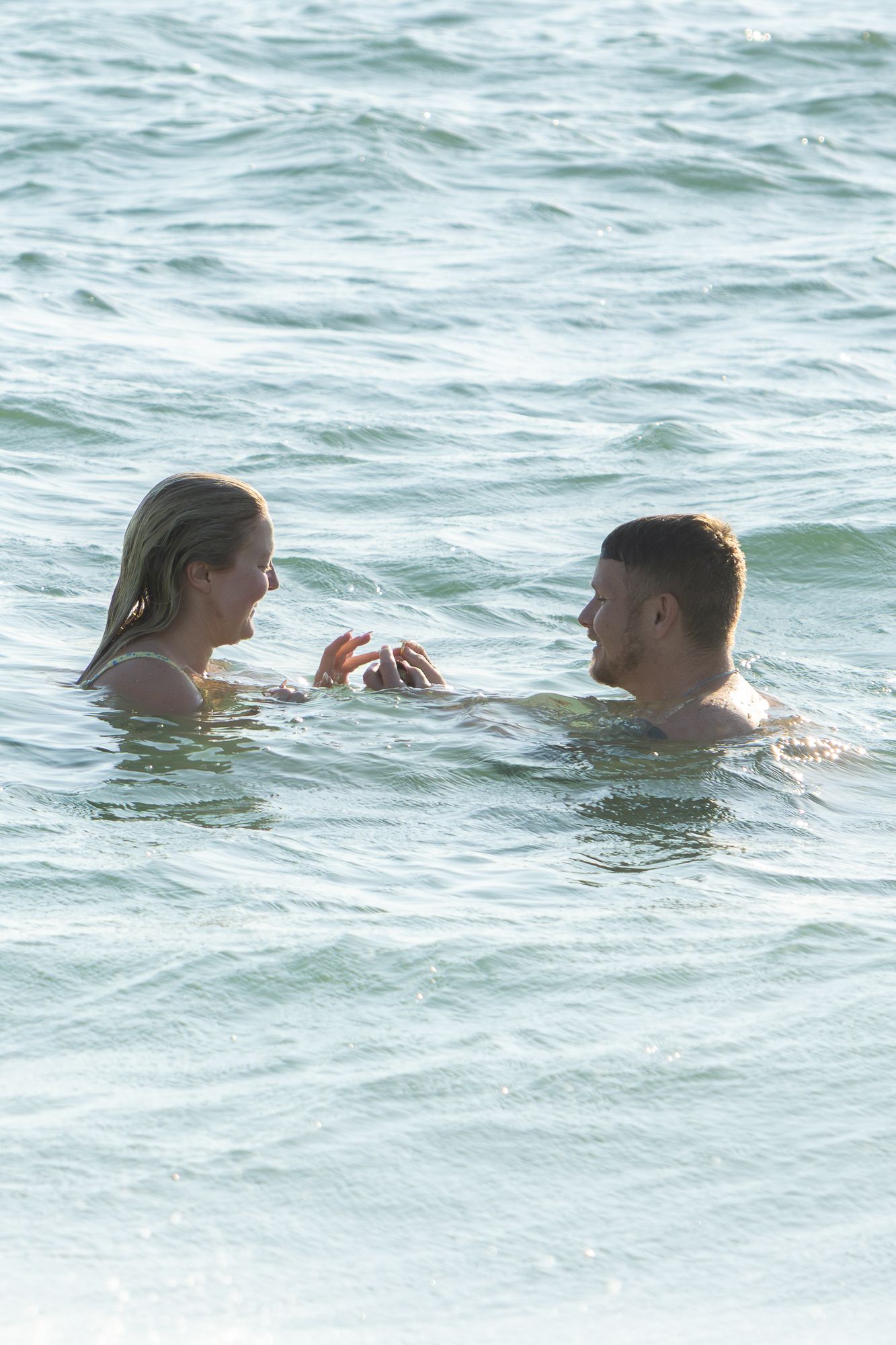 Happy couple facing each other while swimming in ocean waves during romantic beach outing.