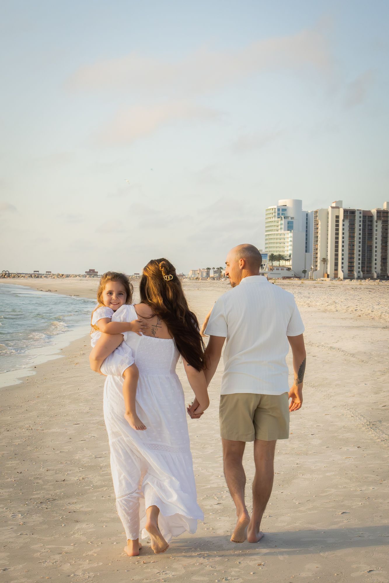 Family in white outfits walking along beach shoreline at golden hour.