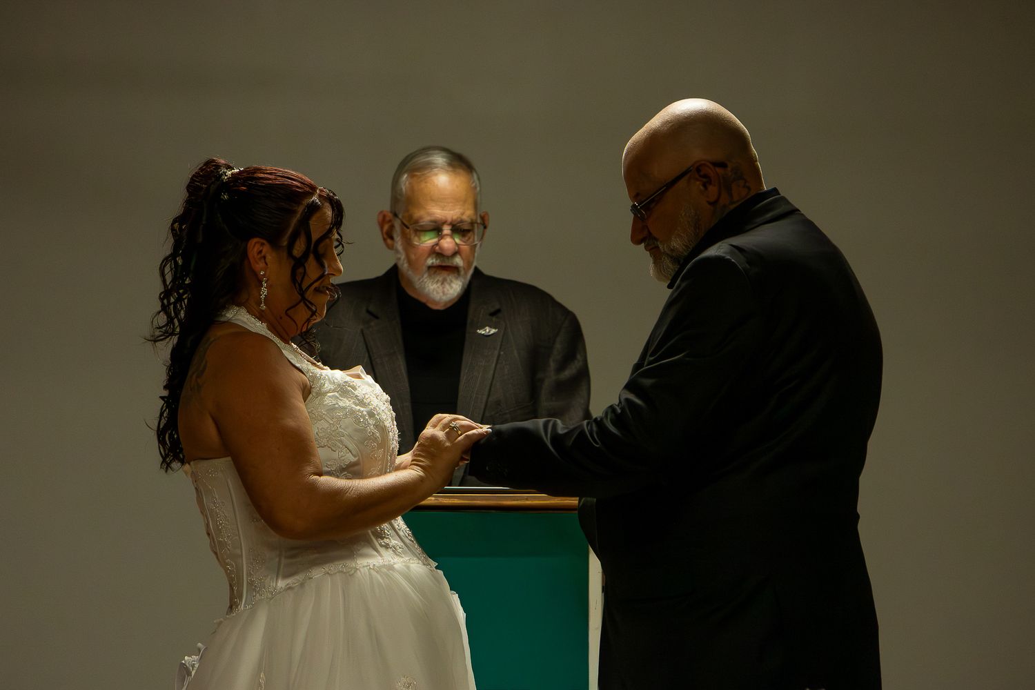 Bride and groom holding hands at altar with officiant during indoor wedding ceremony.