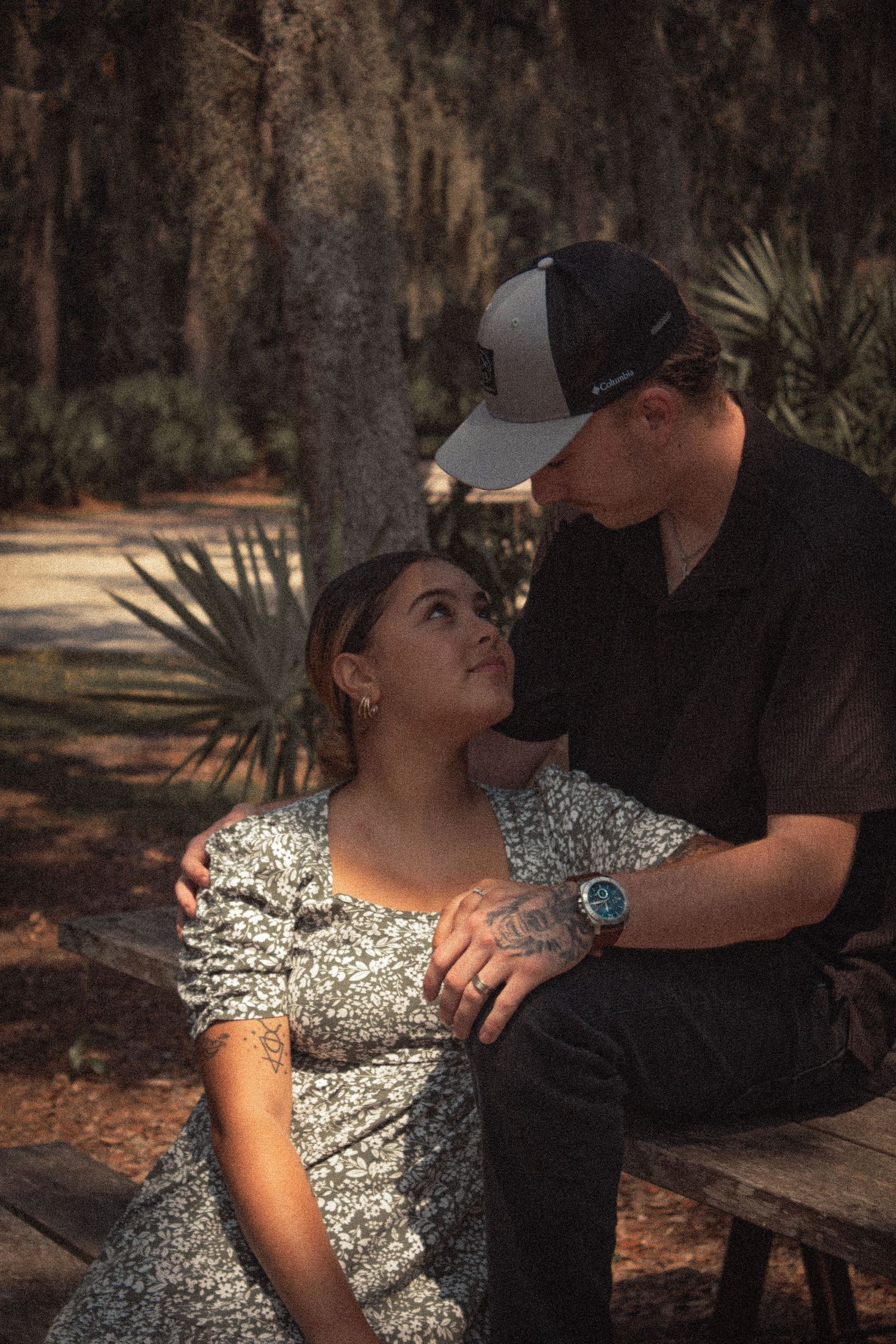 Couple sharing a romantic moment on wooden bench surrounded by Spanish moss trees in shaded forest park.