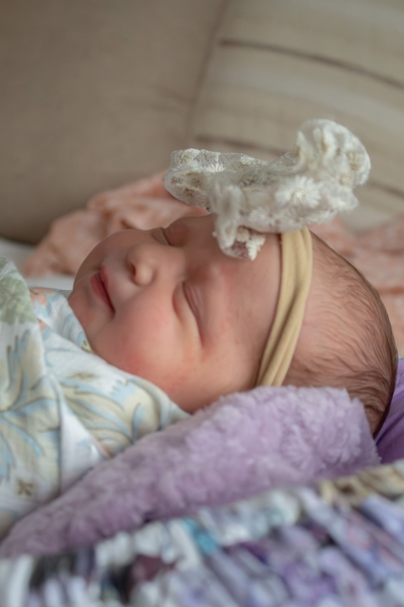 Sleeping newborn baby wearing a white lace headband on a soft blanket.
