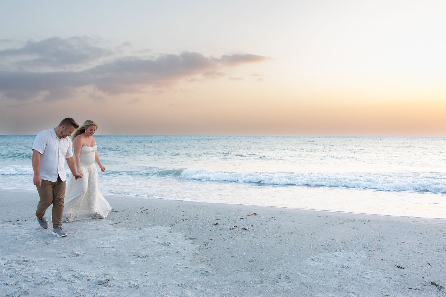 Romantic couple walking hand in hand along a serene beach at dusk with soft pastel sky.