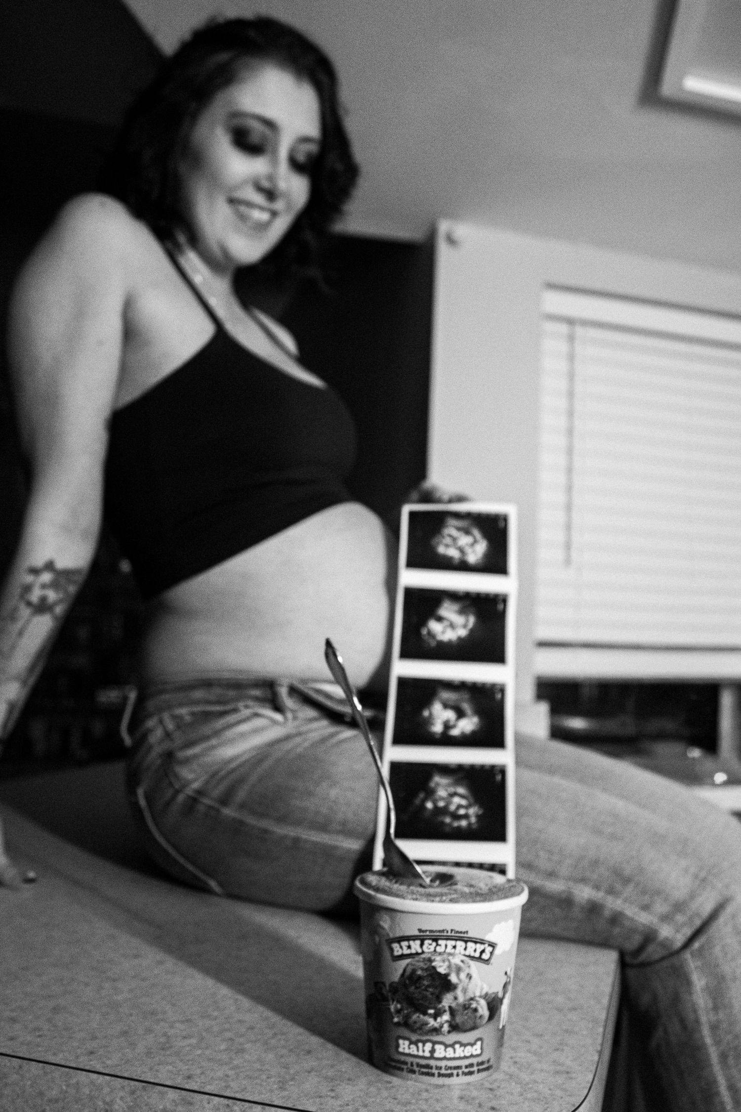 Pregnant woman smiling at Ben & Jerry's Half Baked ice cream and ultrasound photos in black and white photo.