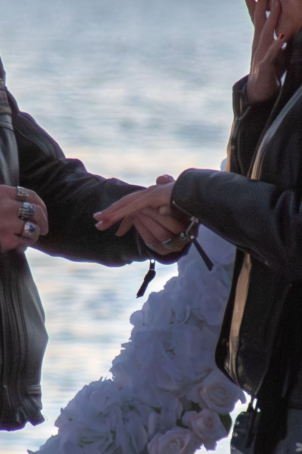 A close-up of a couple holding hands during a marriage proposal near a white floral arrangement.