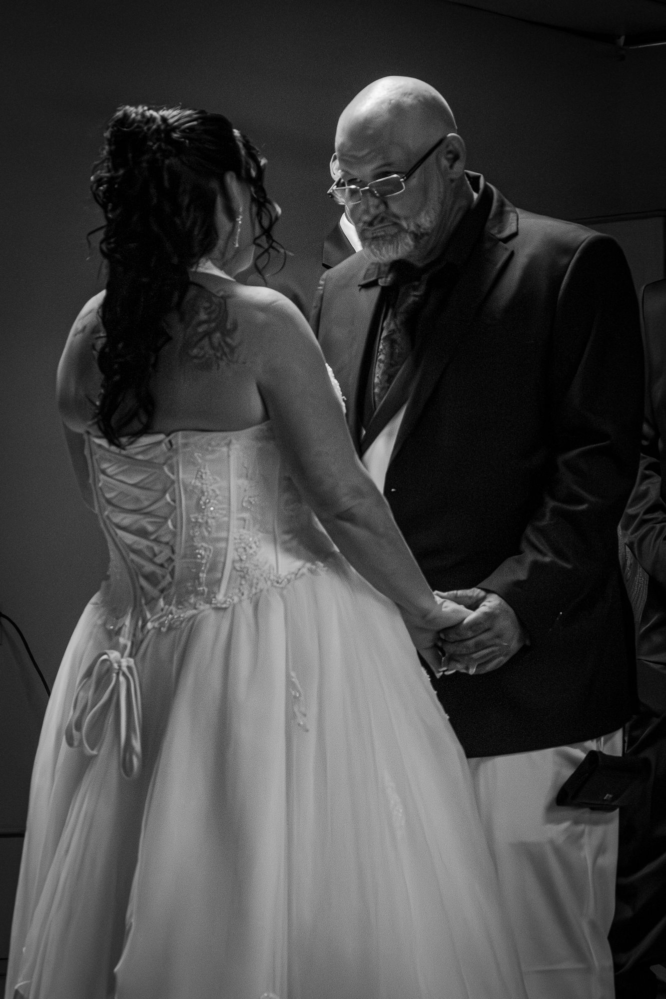 Black and white photo of bride in corset gown and groom holding hands during wedding ceremony.