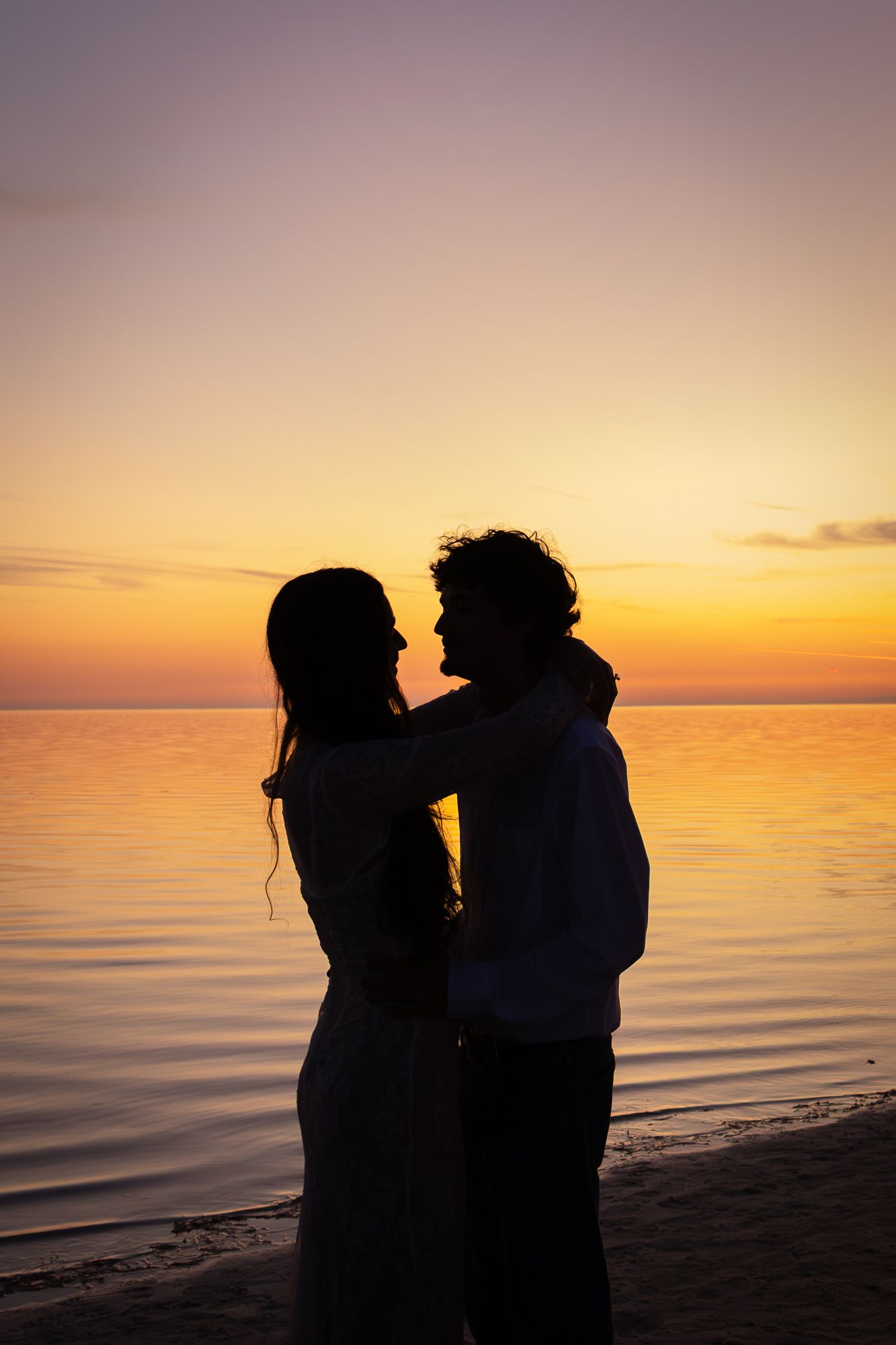 Romantic couple silhouetted against a stunning golden sunset on a calm beach at dusk.
