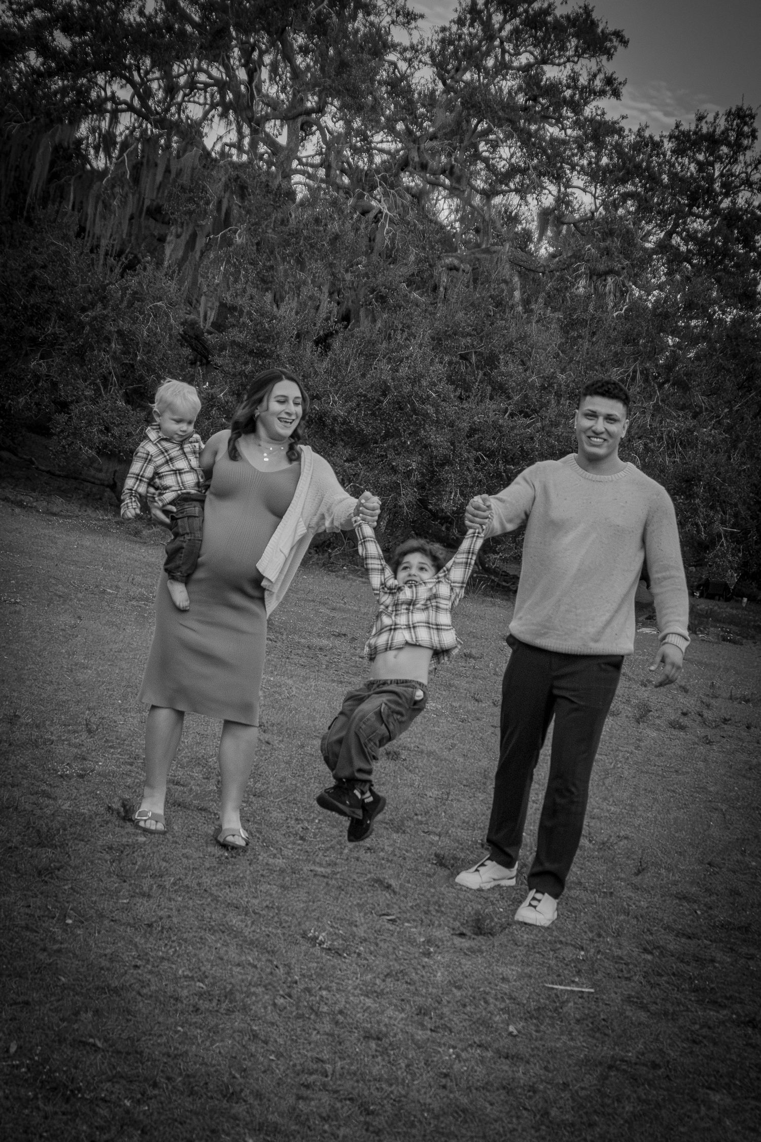 Black and white photo of family swinging young child outdoors in a park.