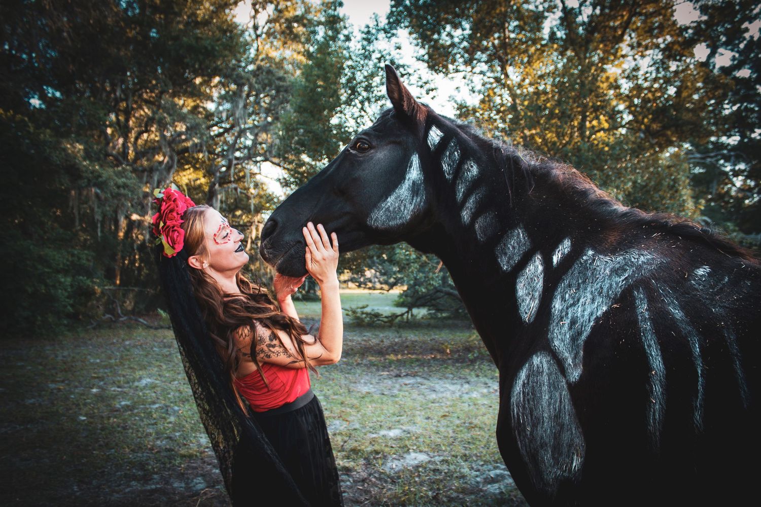 Smiling woman in Day of the Dead costume interacting with black horse in forest.