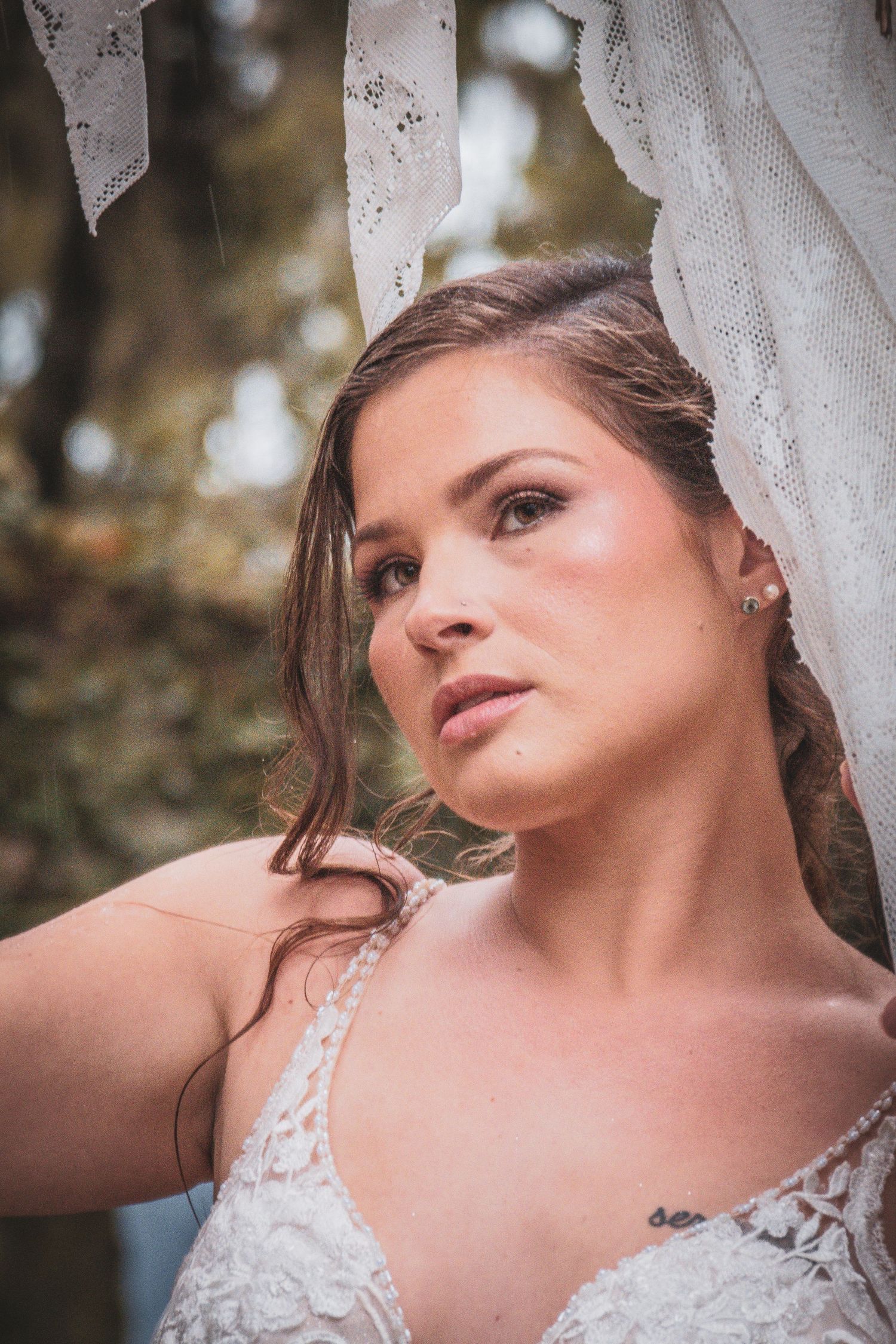 Elegant bride in lace gown gazing upward with soft focus background in outdoor portrait.